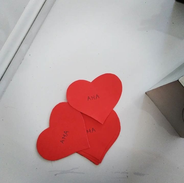 Varios corazones hechos de papel de color rojo con la palabra "AMA" escrita en ellos, colocados sobre una superficie blanca.