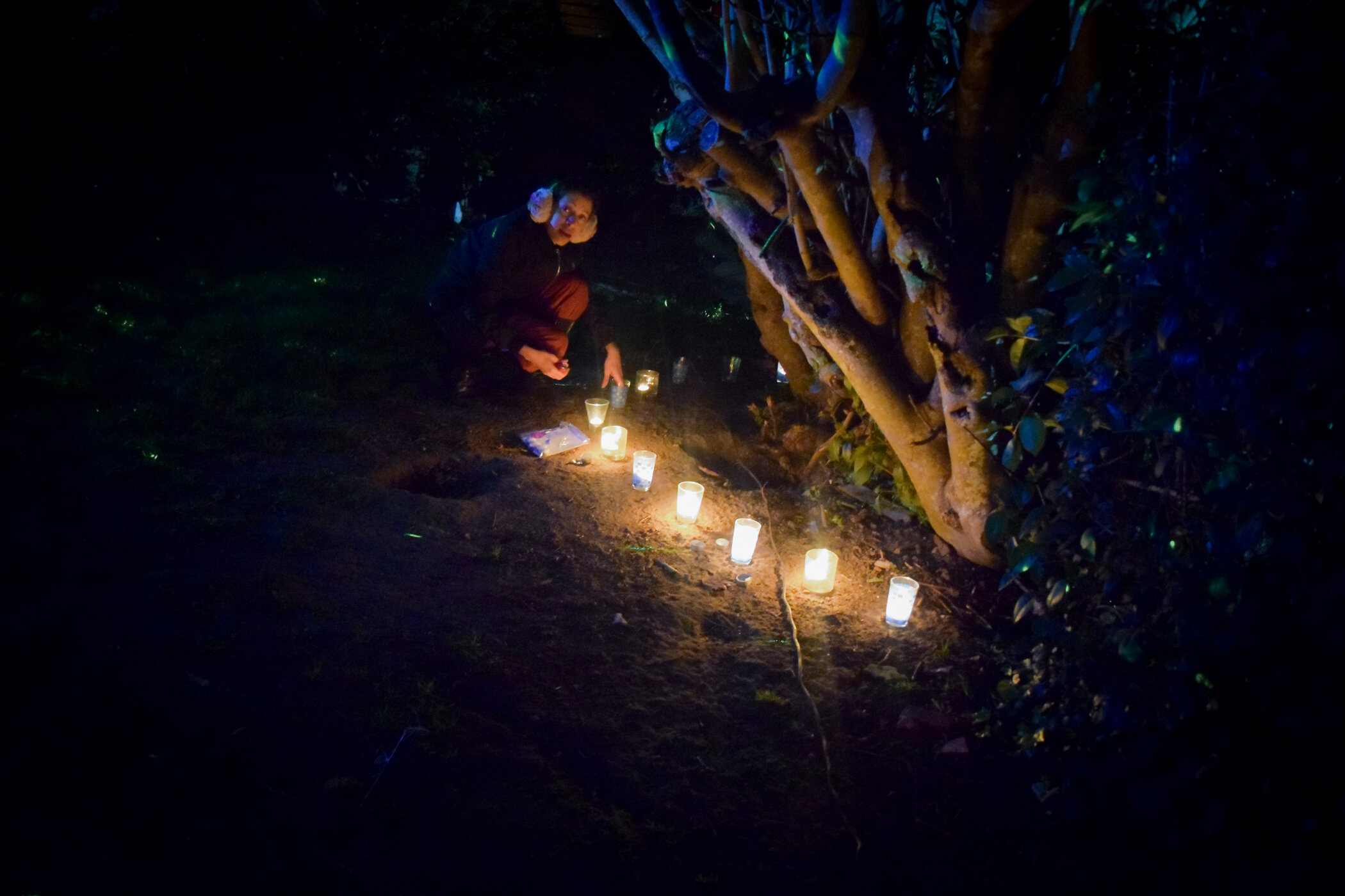 Persona colocando velas encendidas en el suelo en un ambiente oscuro y natural.