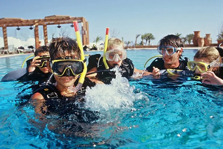 Children wearing snorkeling gear and masks in a swimming pool during daytime.