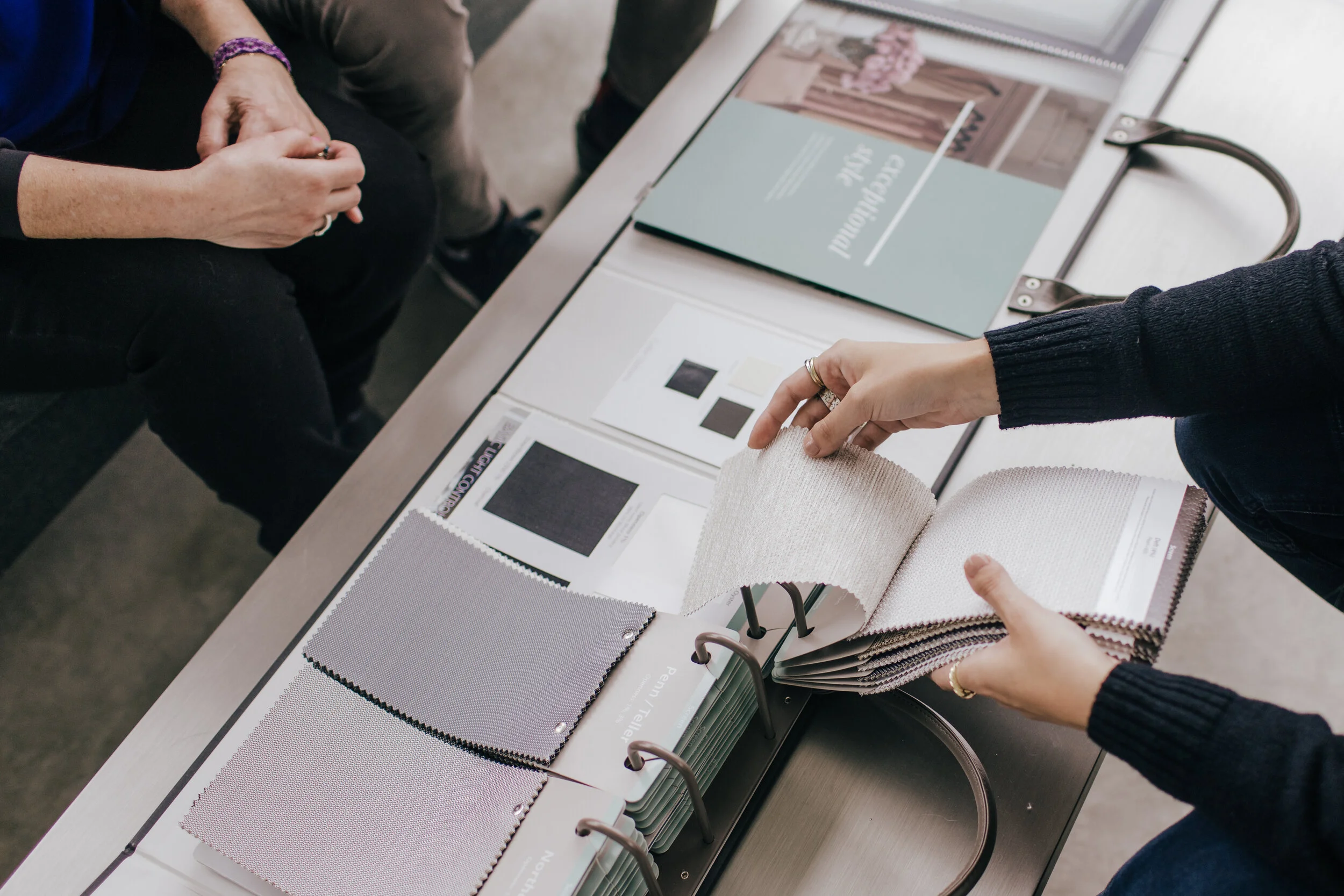 People at a table reviewing fabric swatches, color samples, and a magazine for interior design or upholstery selection.