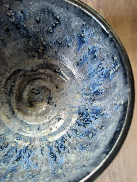 View of a clear glass, likely a drinking glass, with blue and white residue or foam inside, resting on a wooden surface.