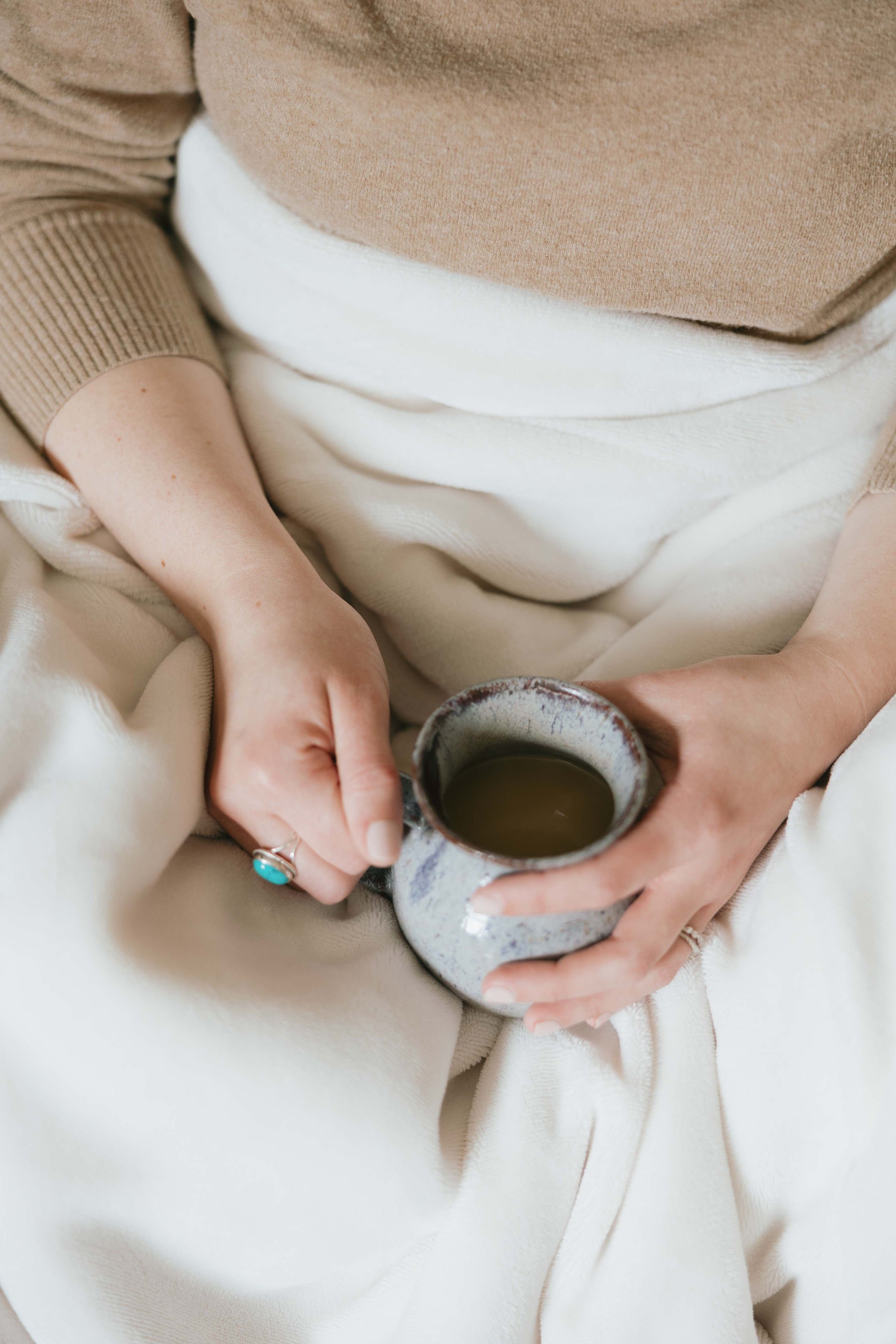 Person wearing beige and white clothing holding a mug of coffee or tea.