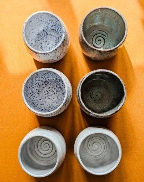 Six ceramic cups with spiral and speckled patterns on a wooden surface.