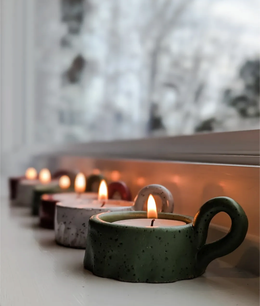 Row of colorful teapot-shaped candles with lit flames on a windowsill.