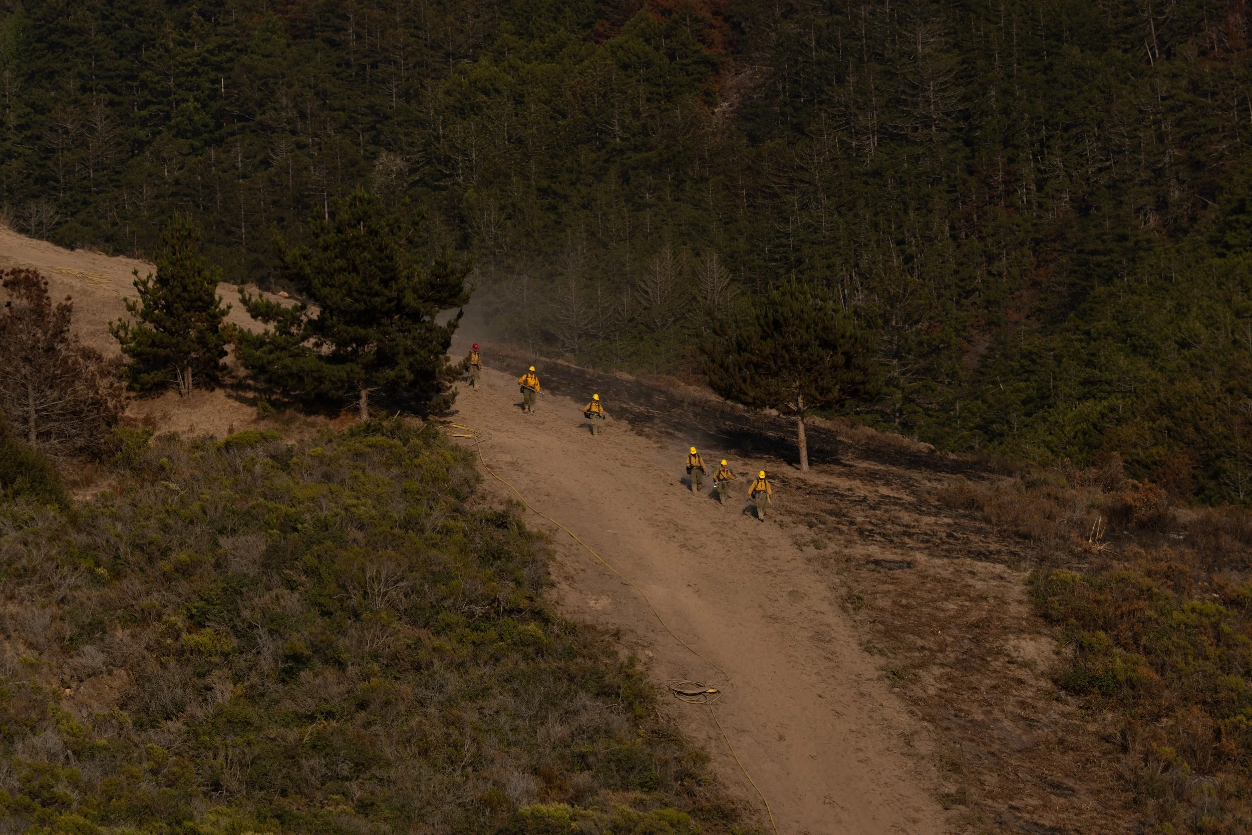 Firefighters walk down a dirt access road after working near an active portion of the Plaskett Fire in Big Sur, Calif., Friday, Sept. 4, 2026.