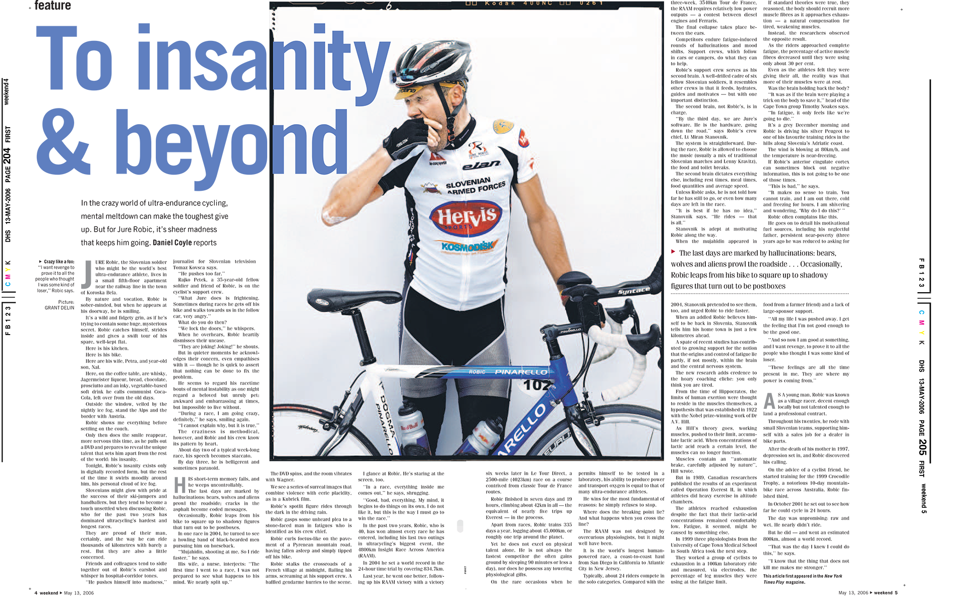 A male cyclist in a white and black cycling outfit with sponsor logos, wearing a helmet and gloves, standing next to his blue and white Pinnarello road bike against a white background.