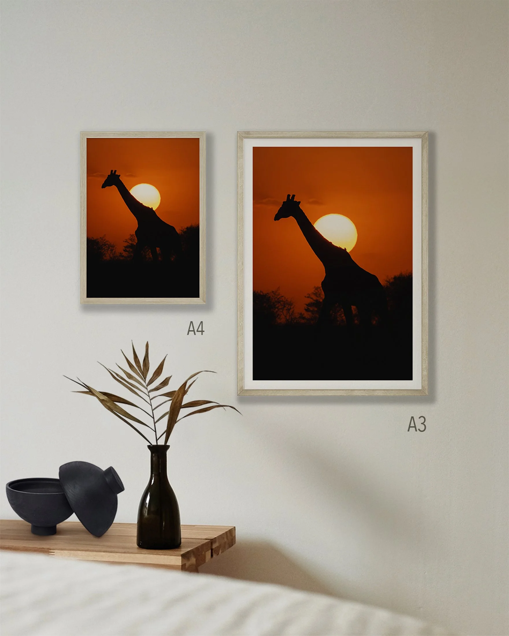 2 prints on a wall of a giraffe silhouette in front of the setting sun. Sizes are A3 and A4.