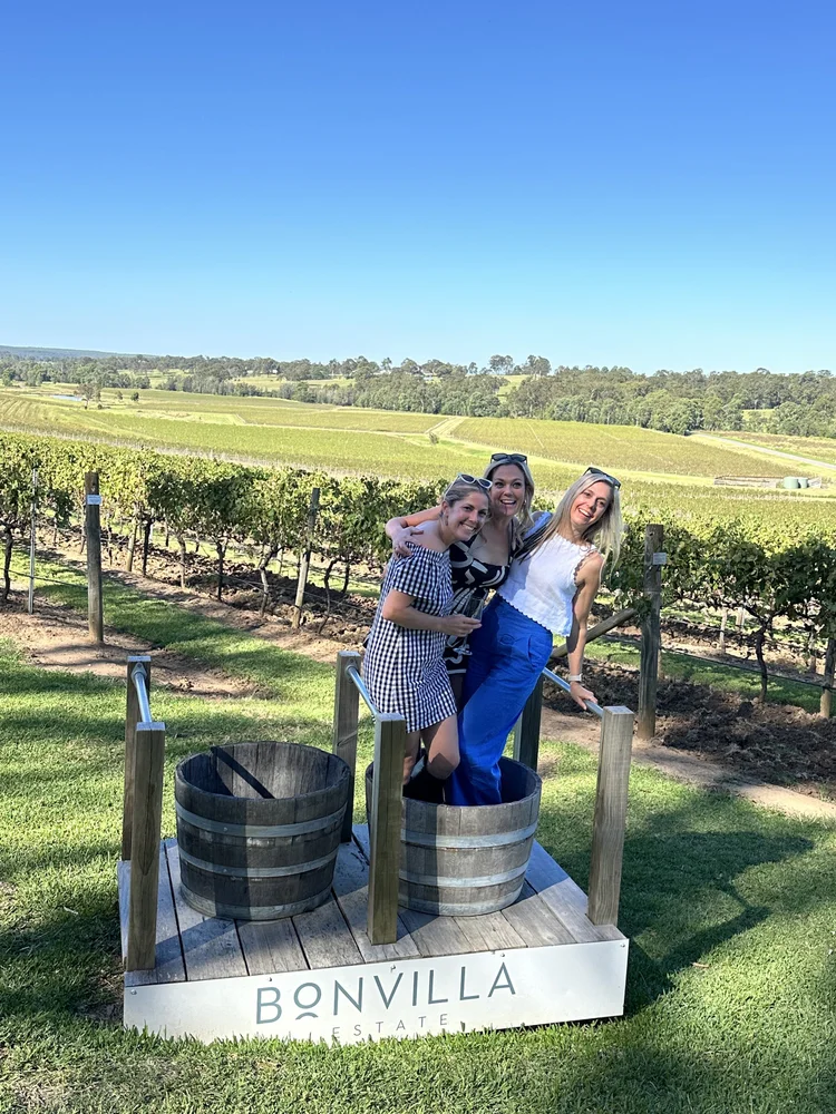 Guests posing beside wine barrels overlooking a vineyard