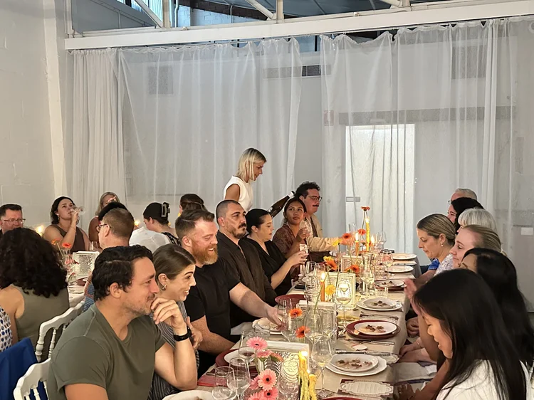 Kat serving wine to guests seated at a long dining table