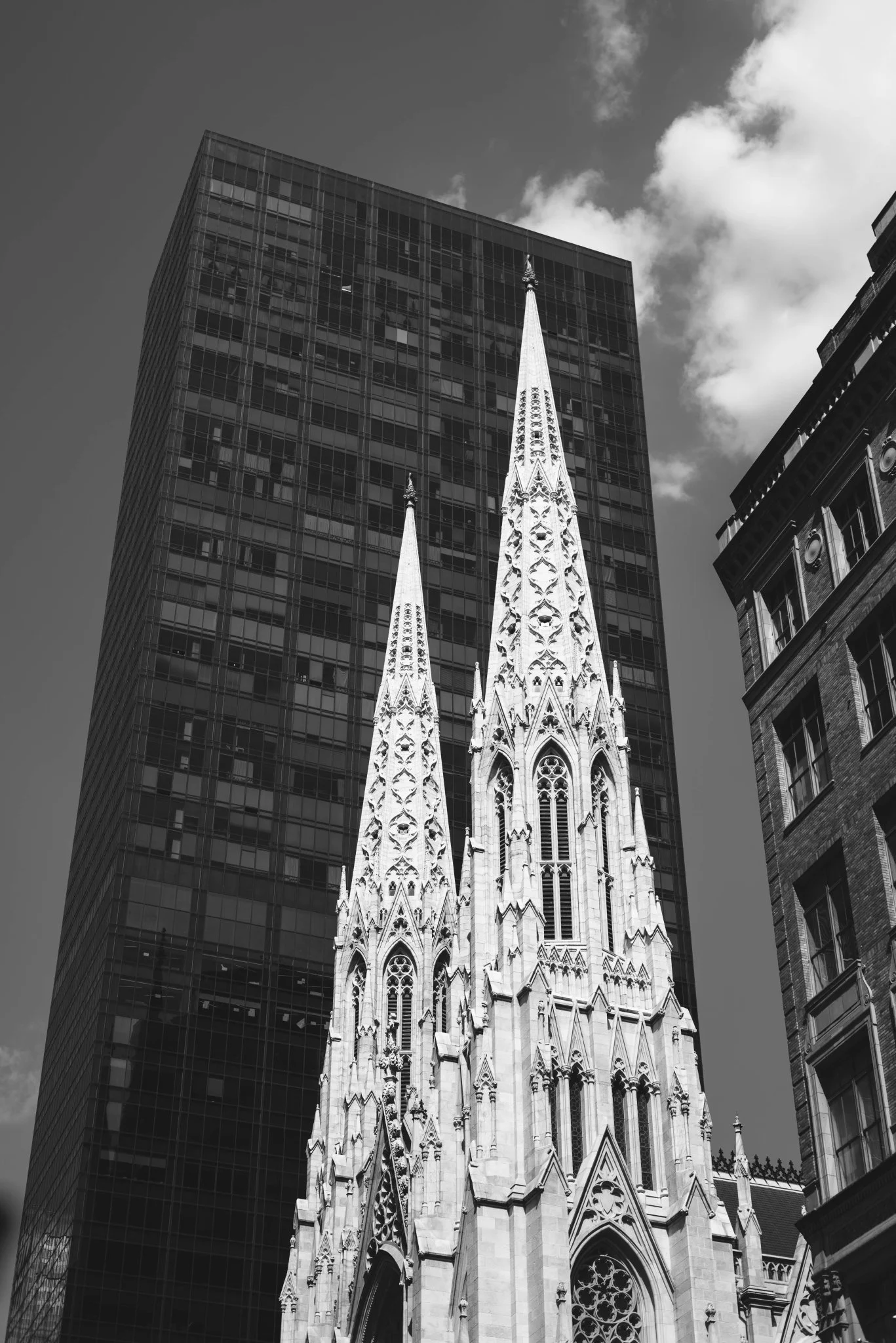 Black and white photo of a Gothic church with tall spires and detailed architecture, surrounded by modern multi-story buildings.