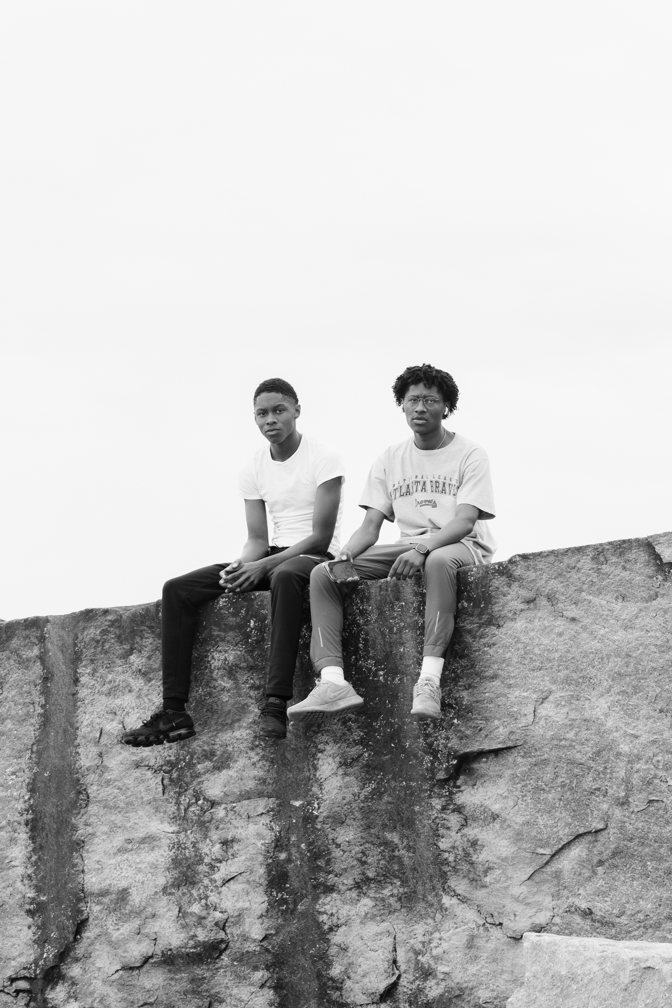 Two young men sitting on a large rock or wall outdoors, black and white photo