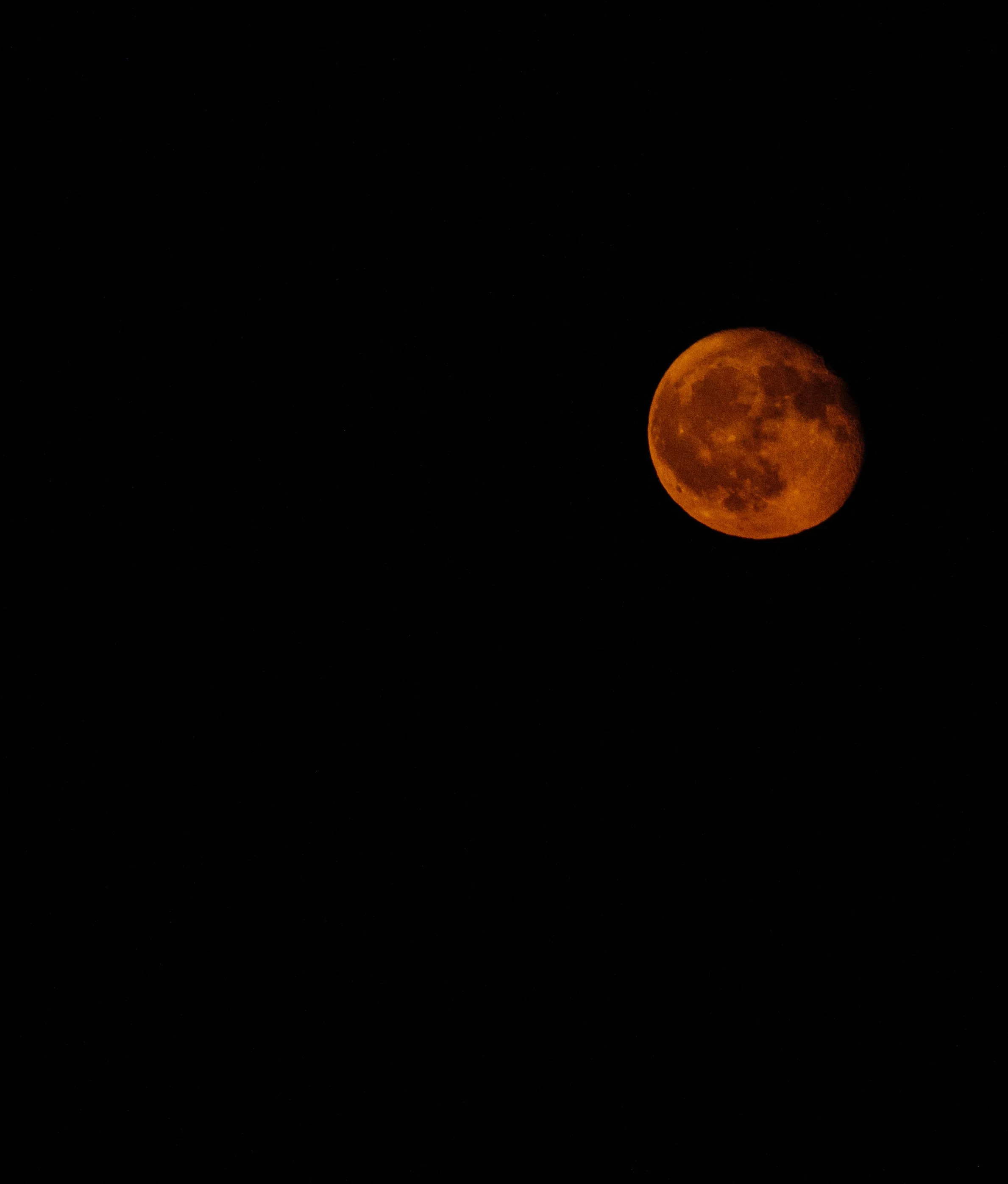 A bright orange full moon against a black night sky.