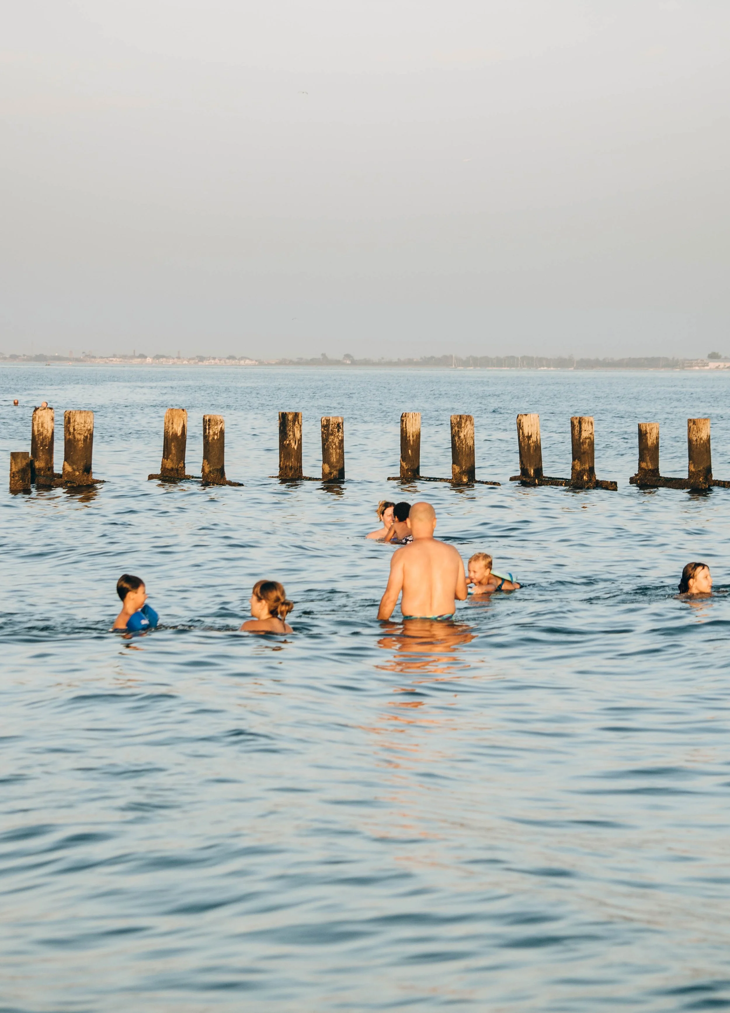 People swimming and relaxing in the sea near wooden posts on a sunny day.