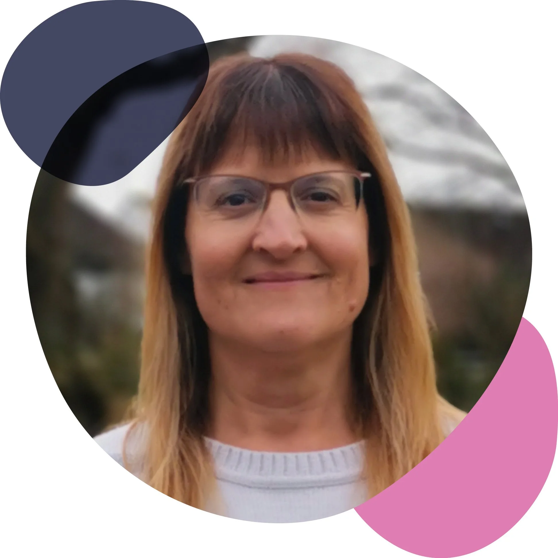 A woman with curly dark hair, blue eyes, and freckles smiling outdoors during daytime, with greenery in the background.