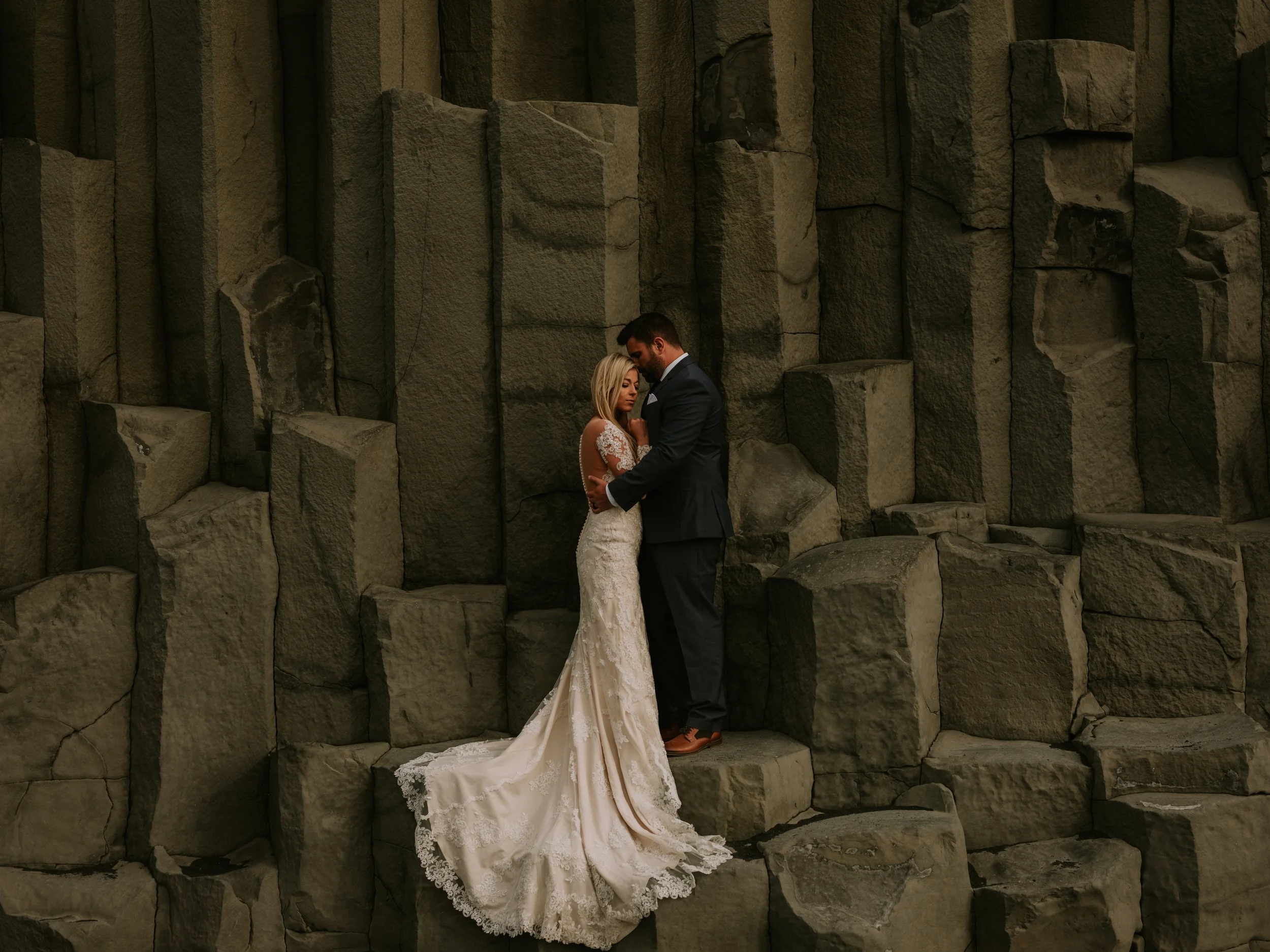 Destination wedding portrait at the black sand beaches of Iceland with bride and groom framed by towering basalt rock formations.