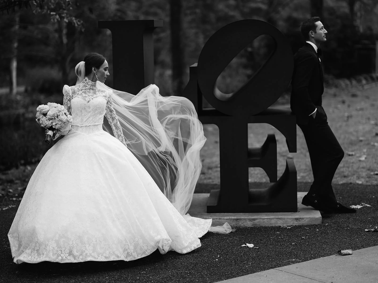 Bride in lace ballgown with flowing veil standing beside LOVE sculpture at Crystal Bridges Museum in Arkansas, photographed by luxury wedding photographer Miles Witt Boyer