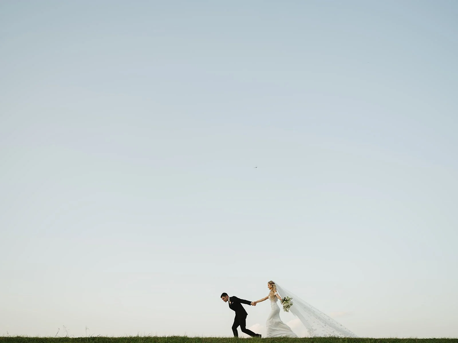 Adventurous Arkansas bride and groom running hand in hand across hilltop at sunset, captured by luxury wedding photographer Miles Witt Boyer