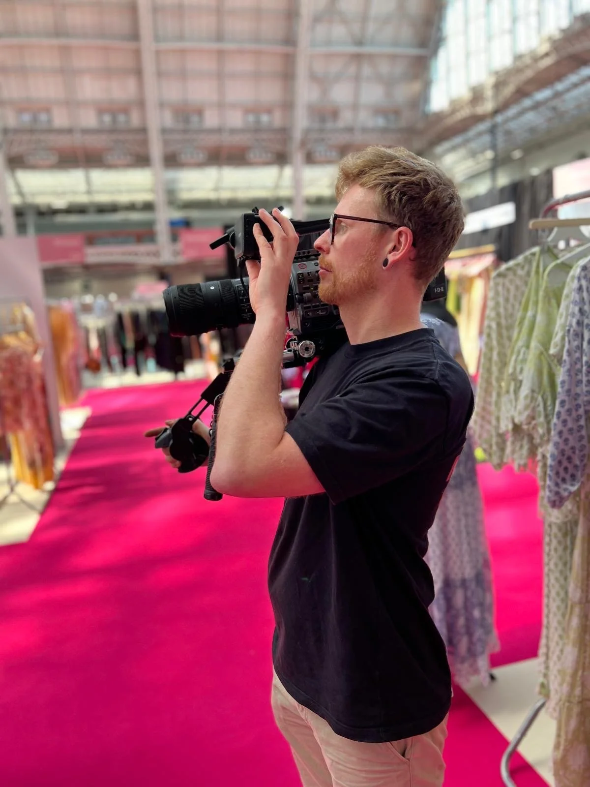 A man is holding a camera on his shoulder at London Olympia and looking through the viewfinder