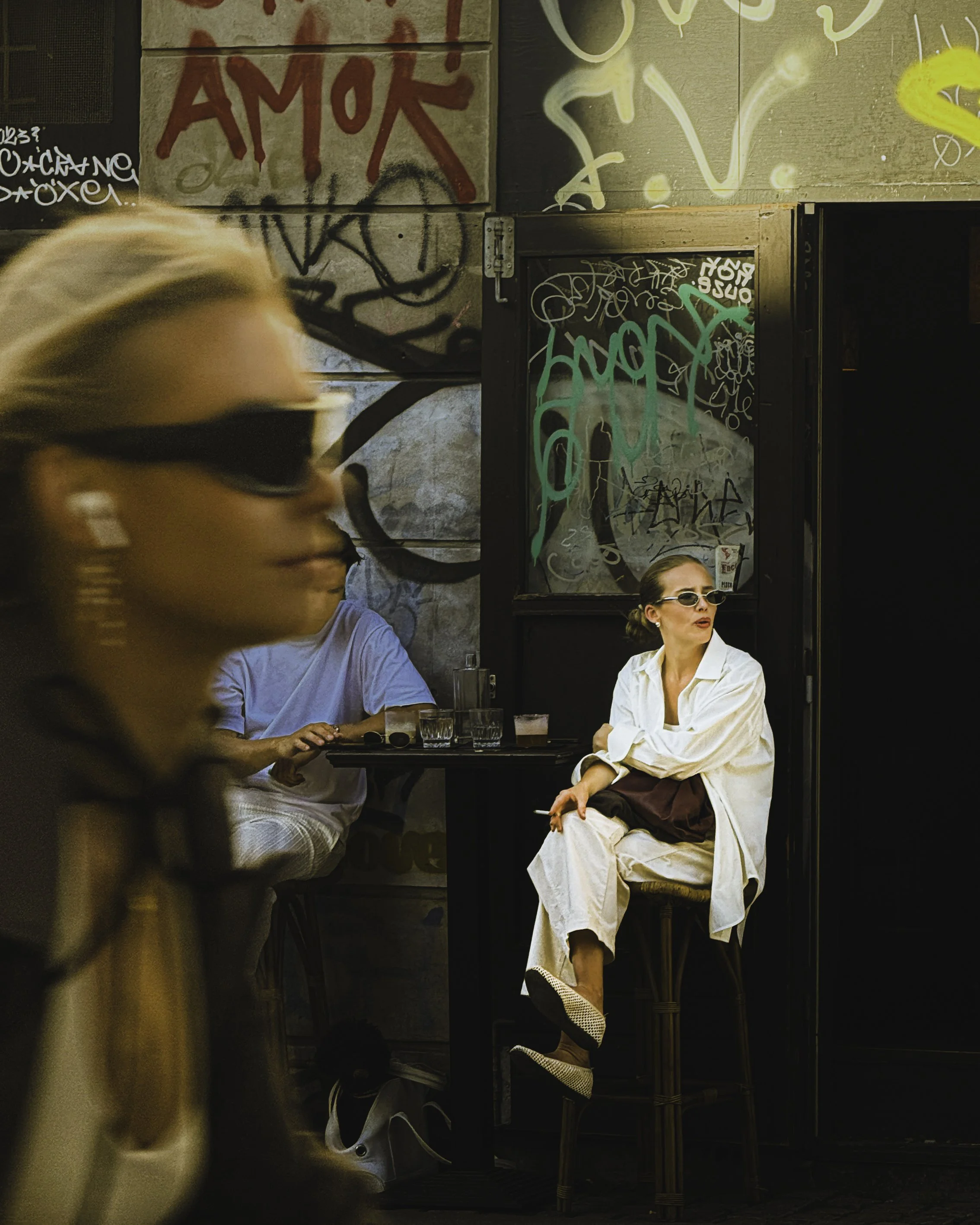 People sitting at an outdoor cafe, with graffiti and artwork on the wall behind them.