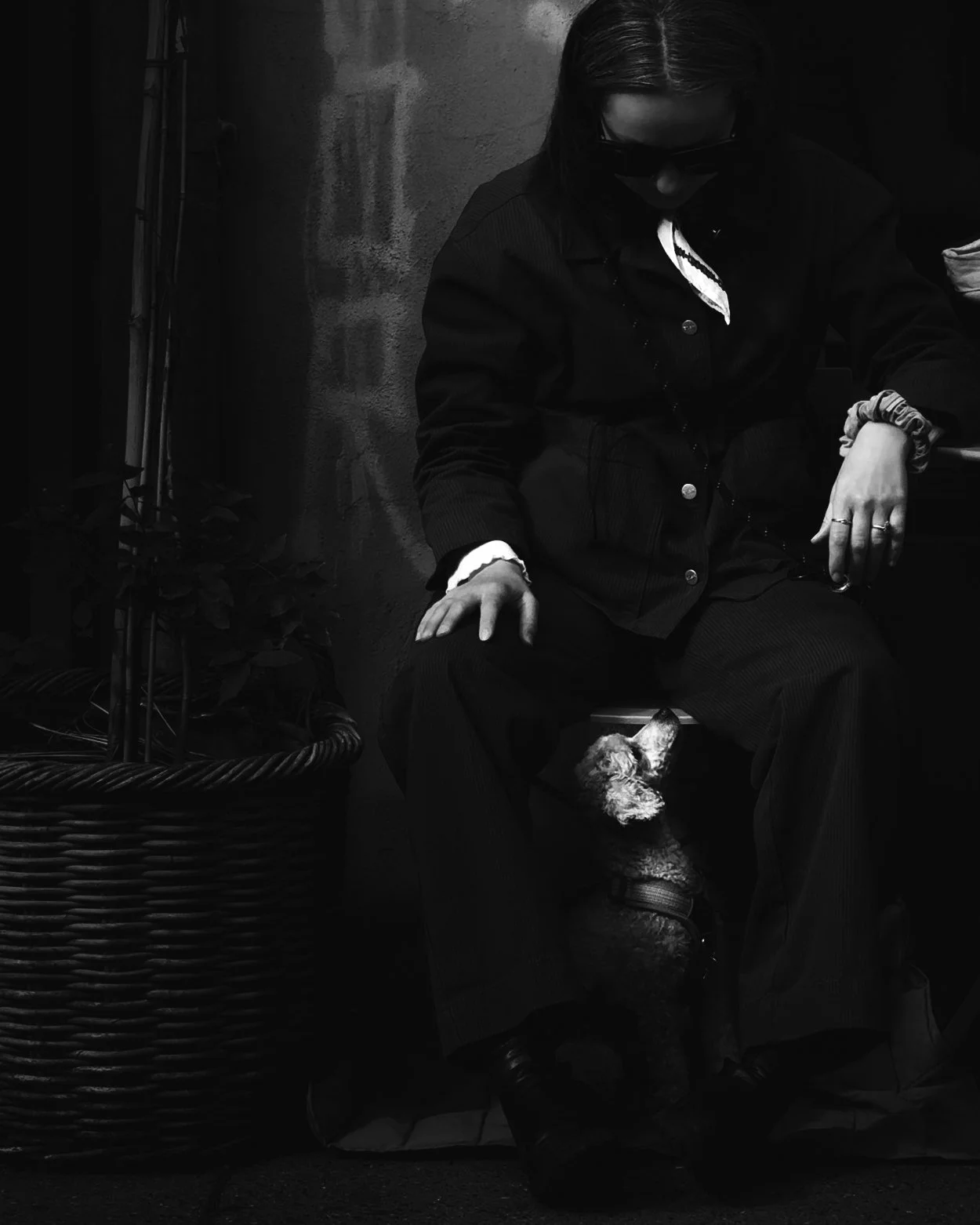 A woman sitting on a chair with a dog near her foot, against a textured wall, in black and white.