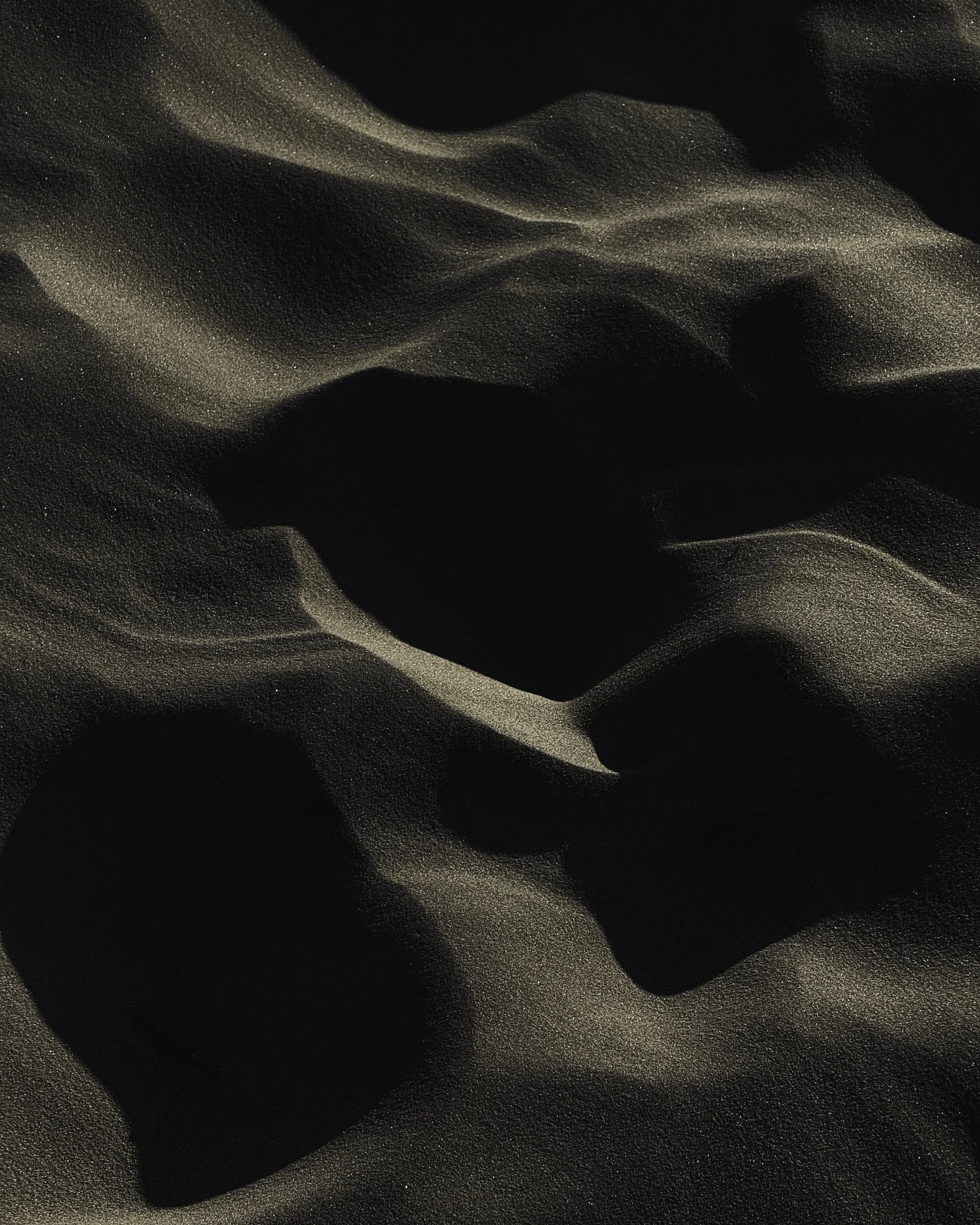 Close-up of sand with a shiny, smooth, and slightly textured appearance, featuring gentle folds and shadows.