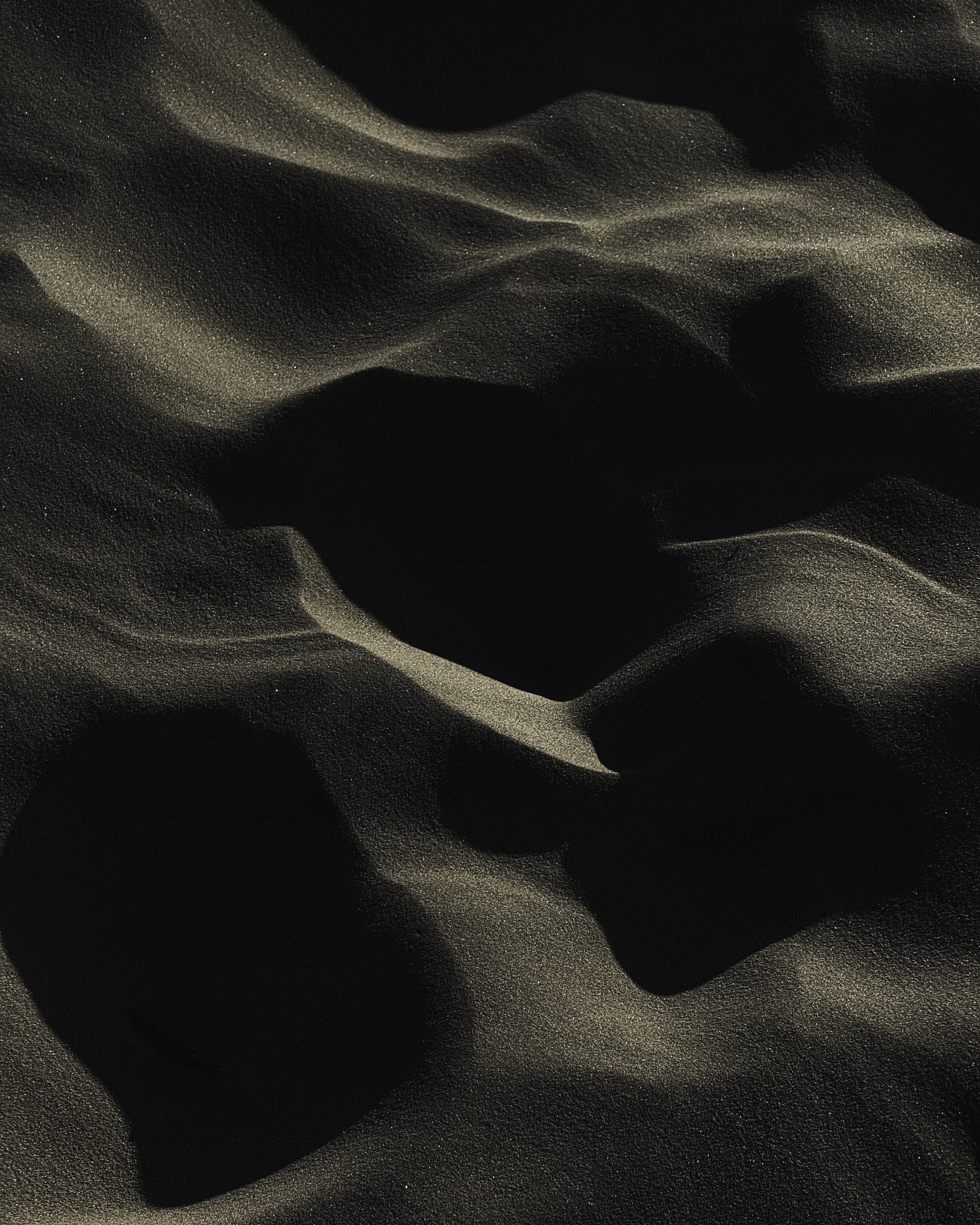 Close-up of dark sand with a shiny, silky texture and subtle highlights.