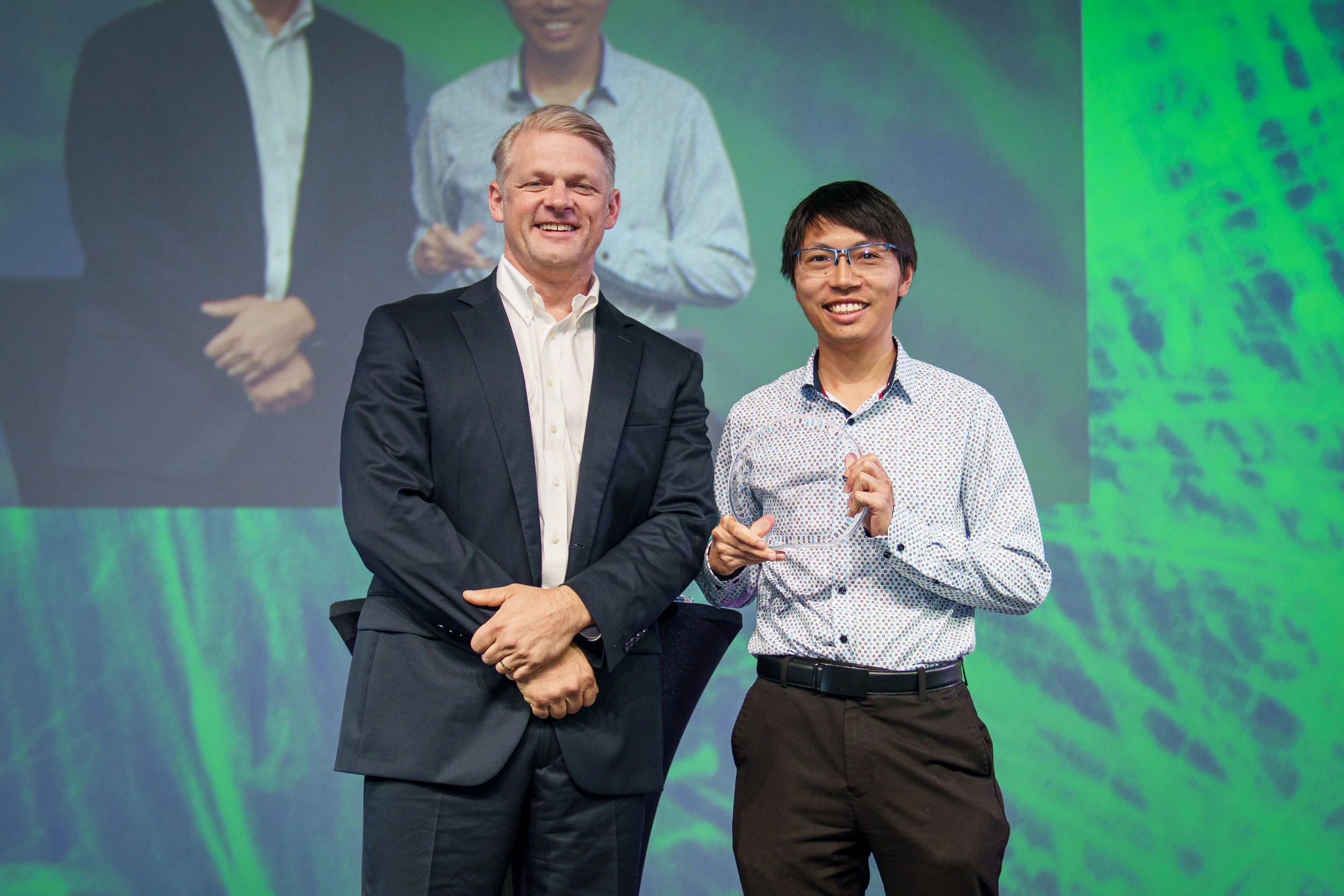 Four people standing on stage in formal attire, with a large screen behind them displaying the words 'International Society of Stem Cell Research' and a green and blue graphic. The woman second from the left is holding an award or trophy.