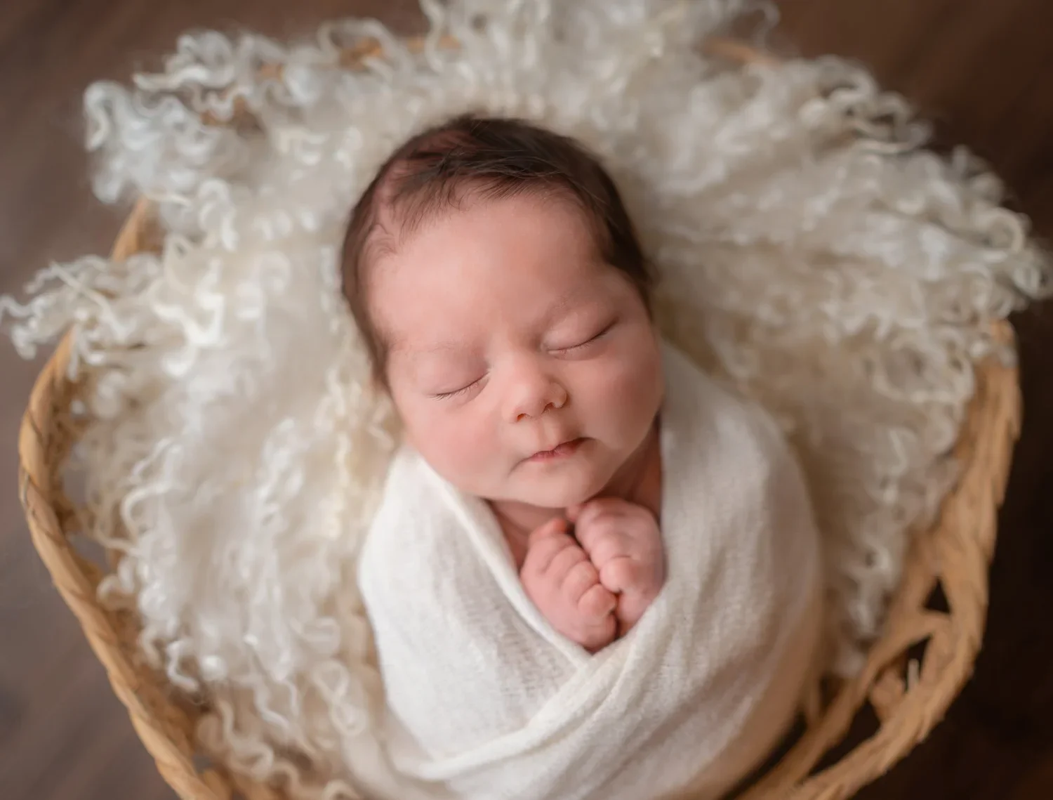 Newborn baby wrapped in blue blanket, sleeping peacefully on a fluffy surface, with a colorful patterned background.