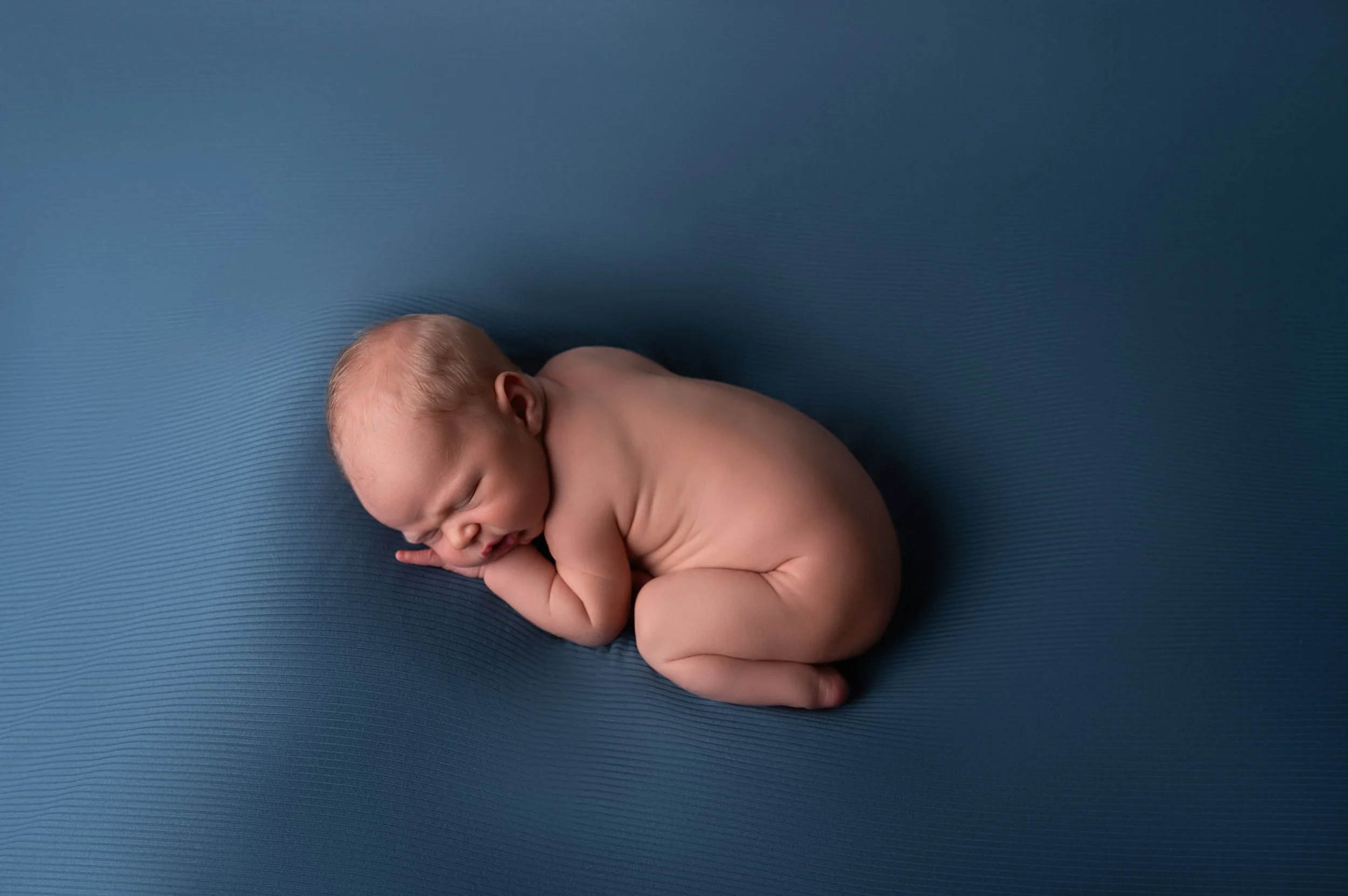 Newborn baby wrapped in blue blanket, sleeping peacefully on a fluffy surface, with a colorful patterned background.