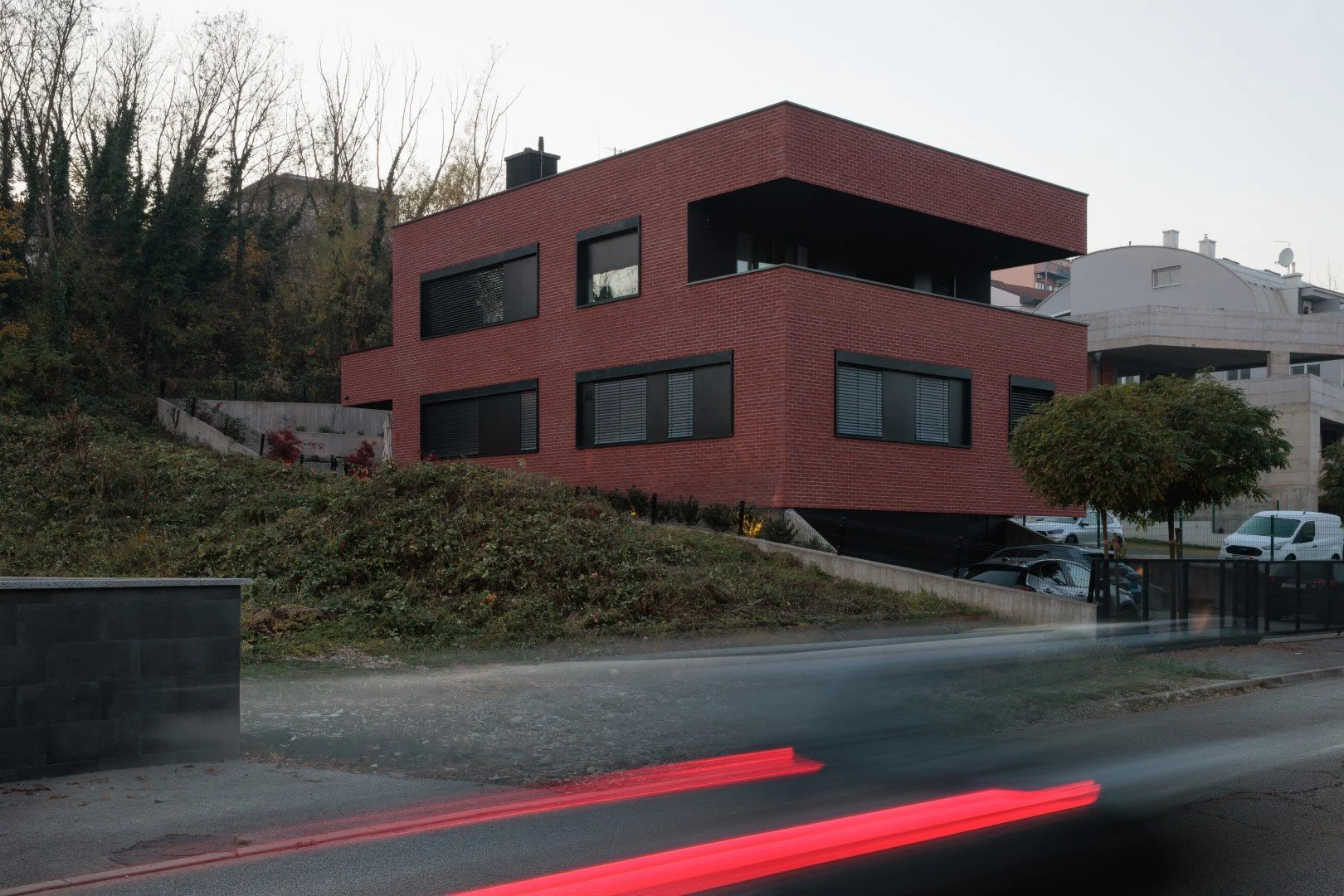 Aruto - mali stambenjak u padini

2019.-2025.

Oblikovanje sklopa kuće i terena proiza&scaron;lo je iz modeliranja topografije i konstruktivnih zahvata za stabilizaciju klizi&scaron;ta. Tamna baza s integriranim garažnim vratima nosi opečni volumen j