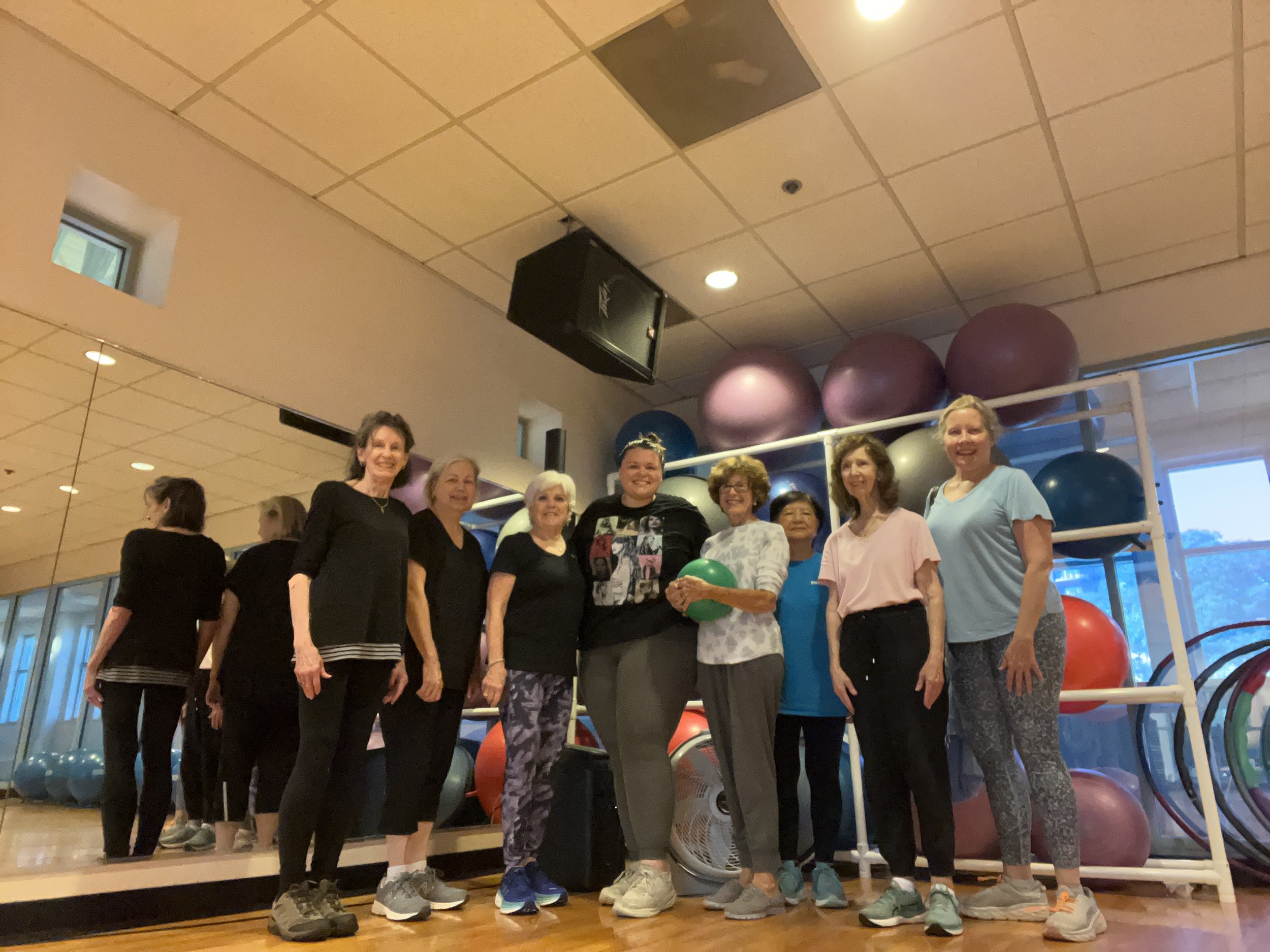 A group of people posing in a fitness studio with exercise balls on shelves.