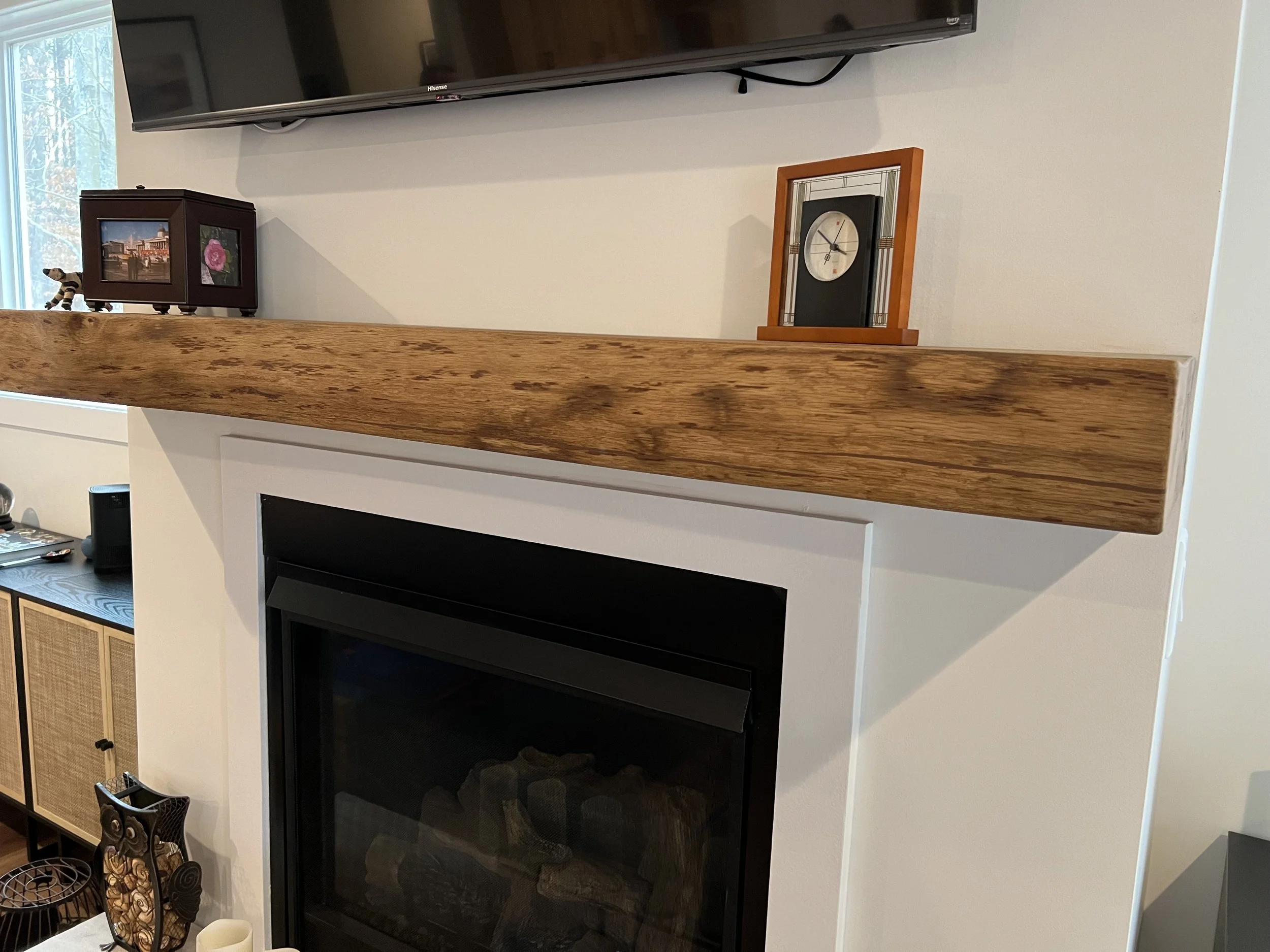 Wooden fireplace mantel with a small picture frame, a clock, and decorative items on top of it in a living room.