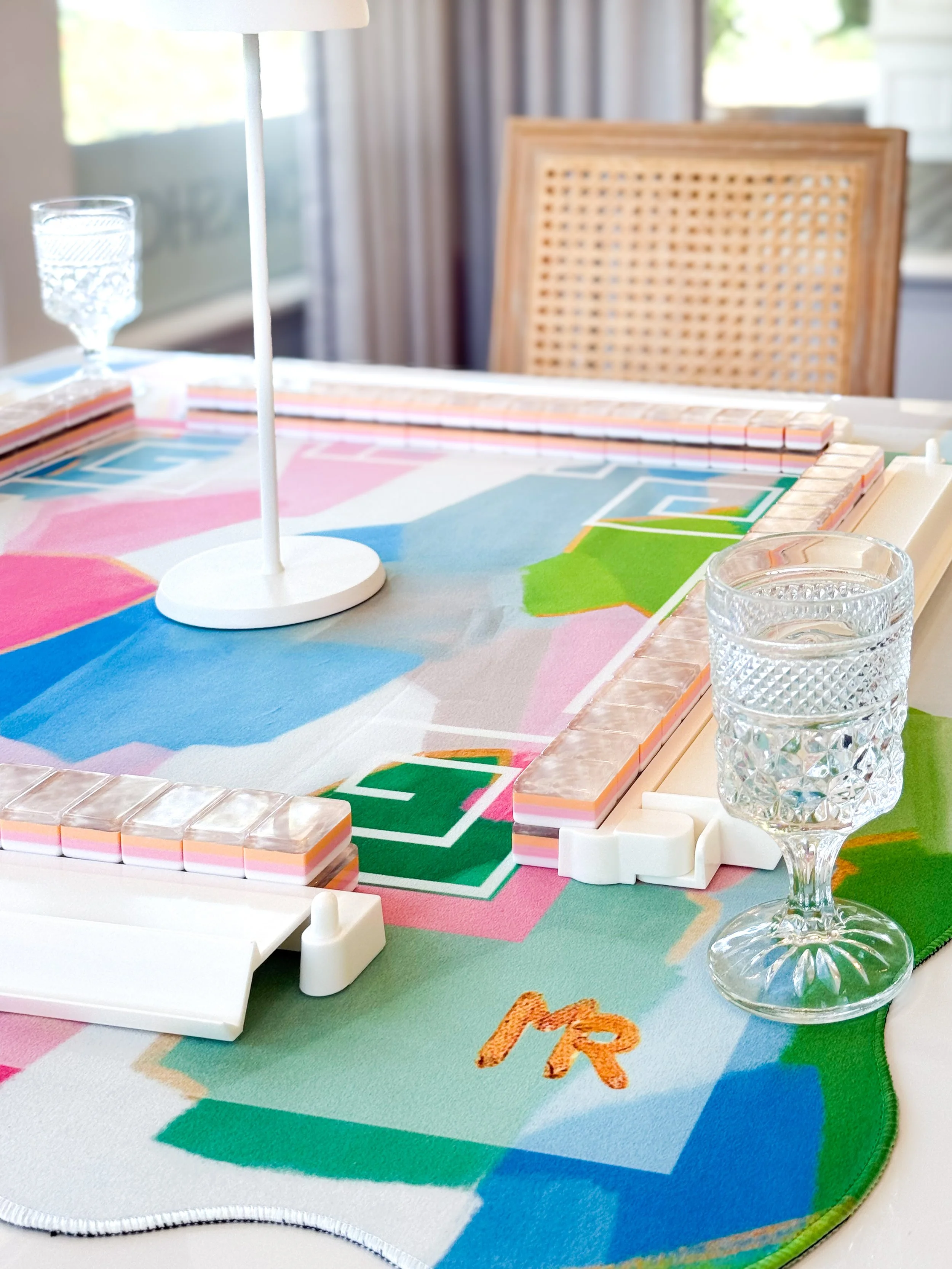 Close-up of a tabletop board game on a colorful rug with glasses of water and a wooden chair in the background.