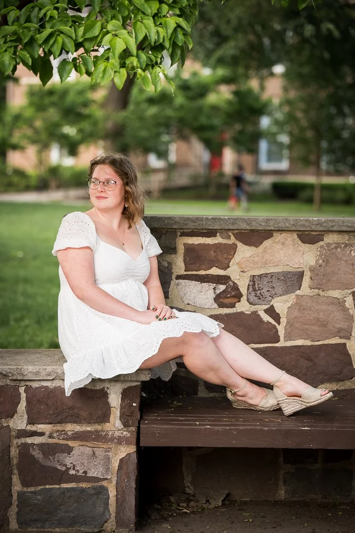  outdoor senior portrait sitting on rock in white dress with greenery background 