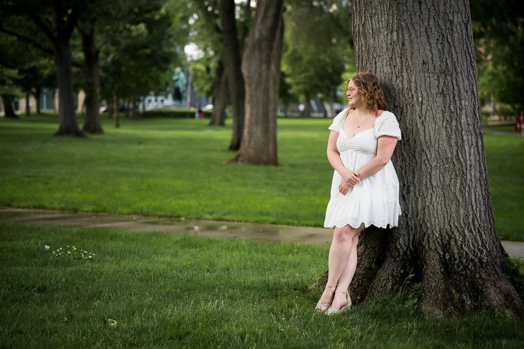  senior graduation photos of college graduate leaning against tree on campus 