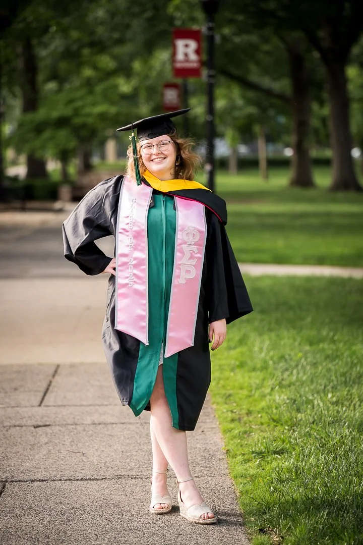  college graduate in cap and gown walking on campus path smiling 