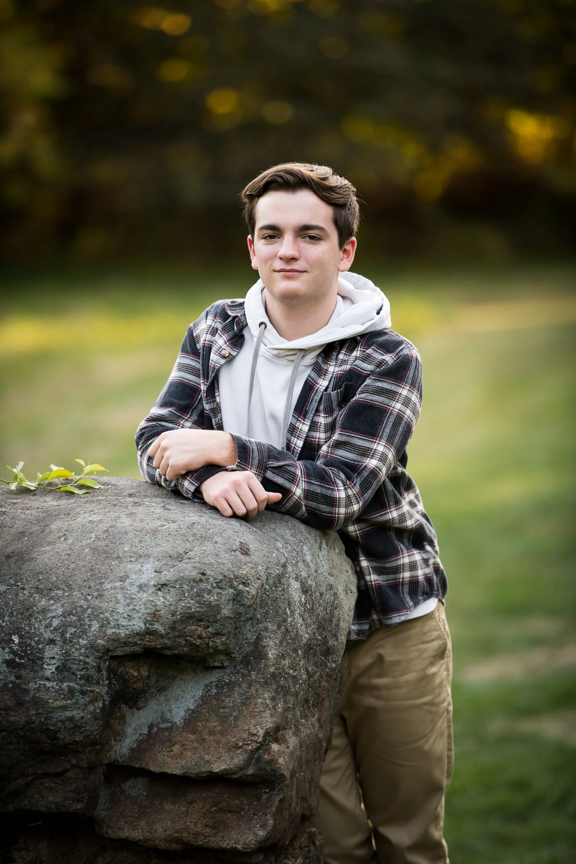  high school senior portraits of male graduate leaning on stone wall outdoors 