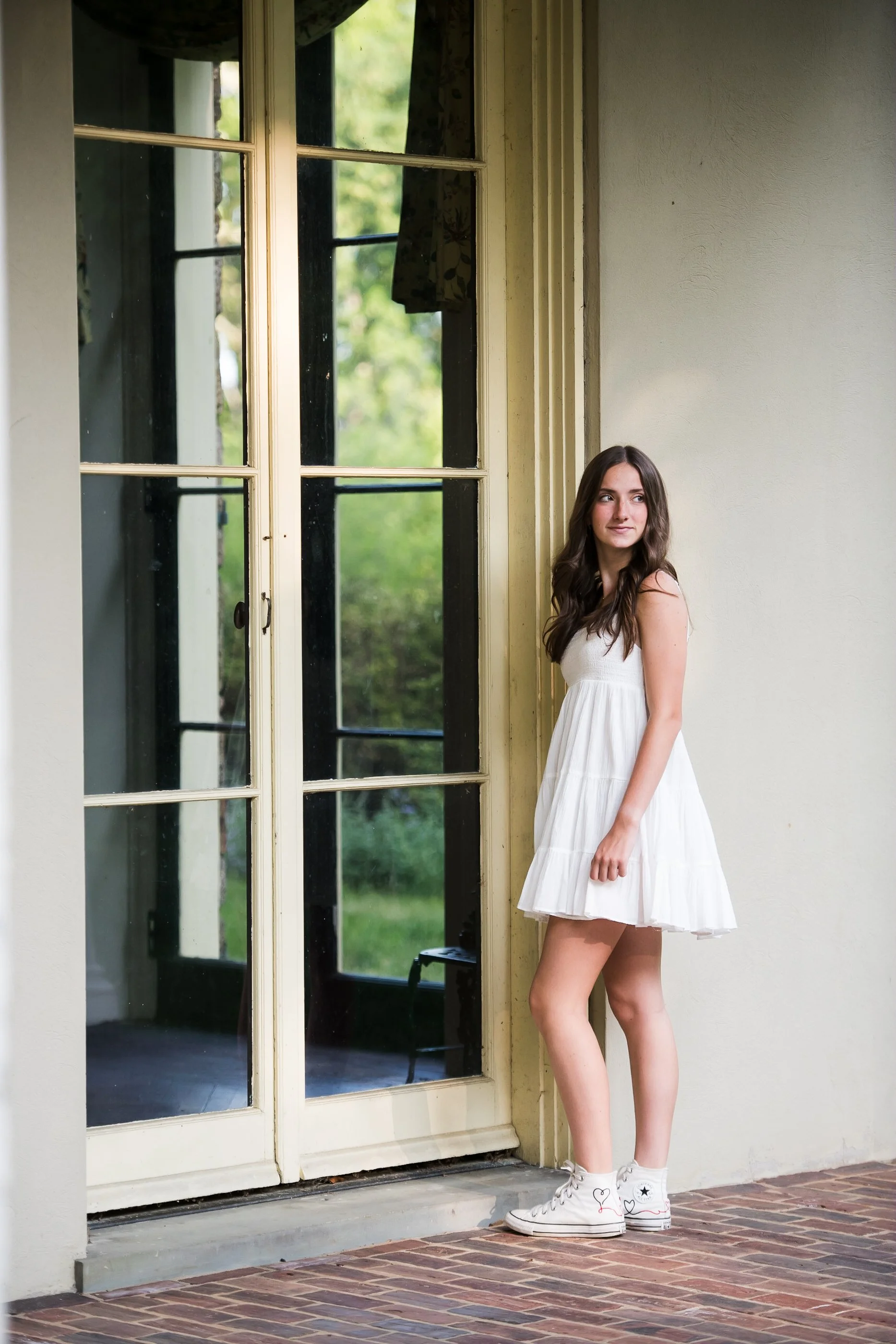  lifestyle senior portrait standing by window in white dress with soft light 