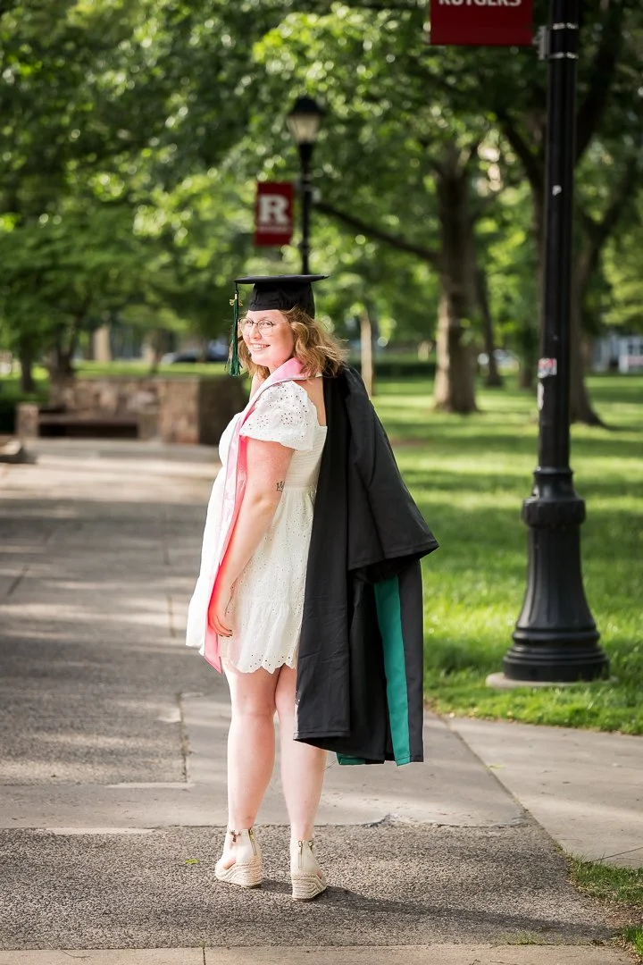 college graduate in cap and gown walking on campus path smiling