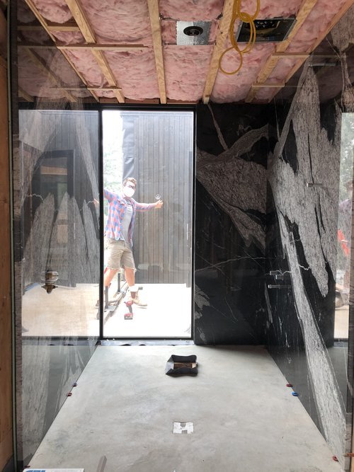 A during construction photo looking past a large black and white marble wall through a glass door to the outside