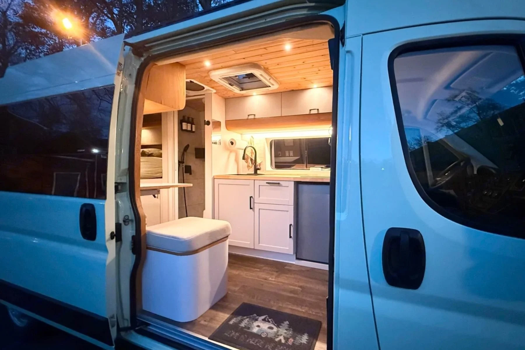 Best-rated custom conversion van in Virginia, a 2021 Dodge ProMaster 3500 with modern wood-accent interior, kitchenette, overhead lighting, and cozy sleeping area.
