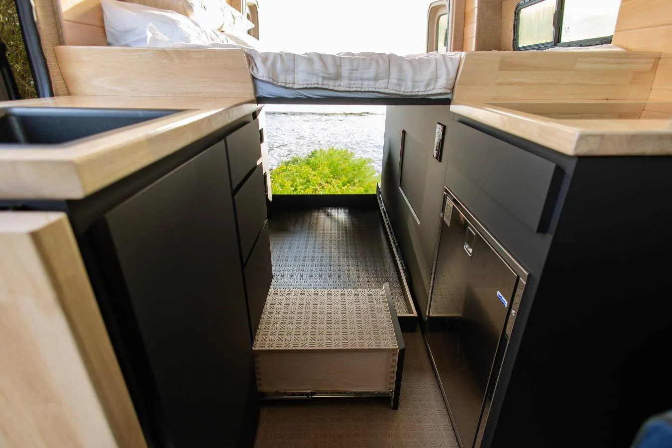 Compact galley kitchen layout with cabinet drawer step and fridge in luxury camper van interior.
