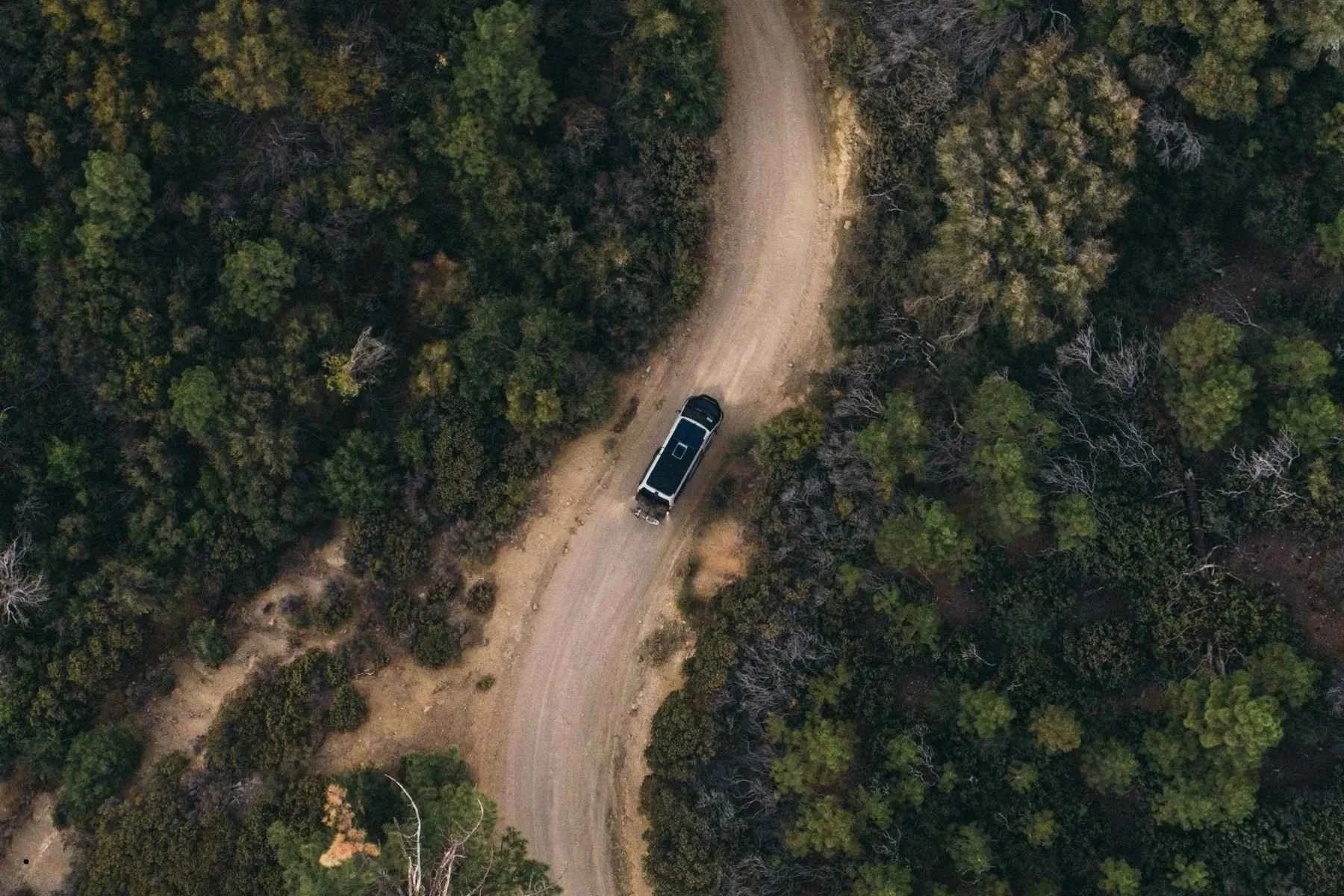 give me alt text for this image. mention sportsmobile3:18 PMAerial view of a Sportsmobile camper van driving a remote dirt road through dense forest on an off-road adventure
