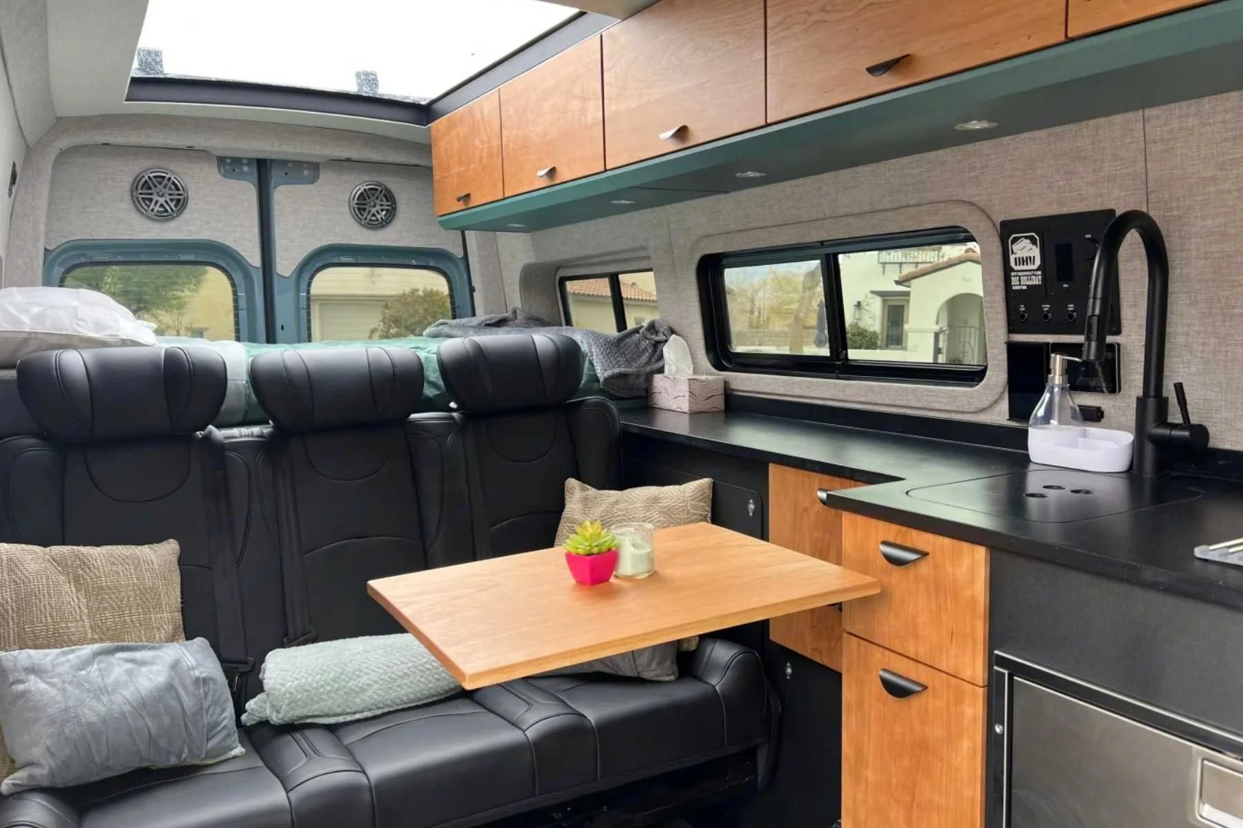 Interior of a Mercedes Sprinter group camper van rental in Las Vegas featuring seating for five, a dining table, wood cabinetry, and a full kitchen for large group road trips.
