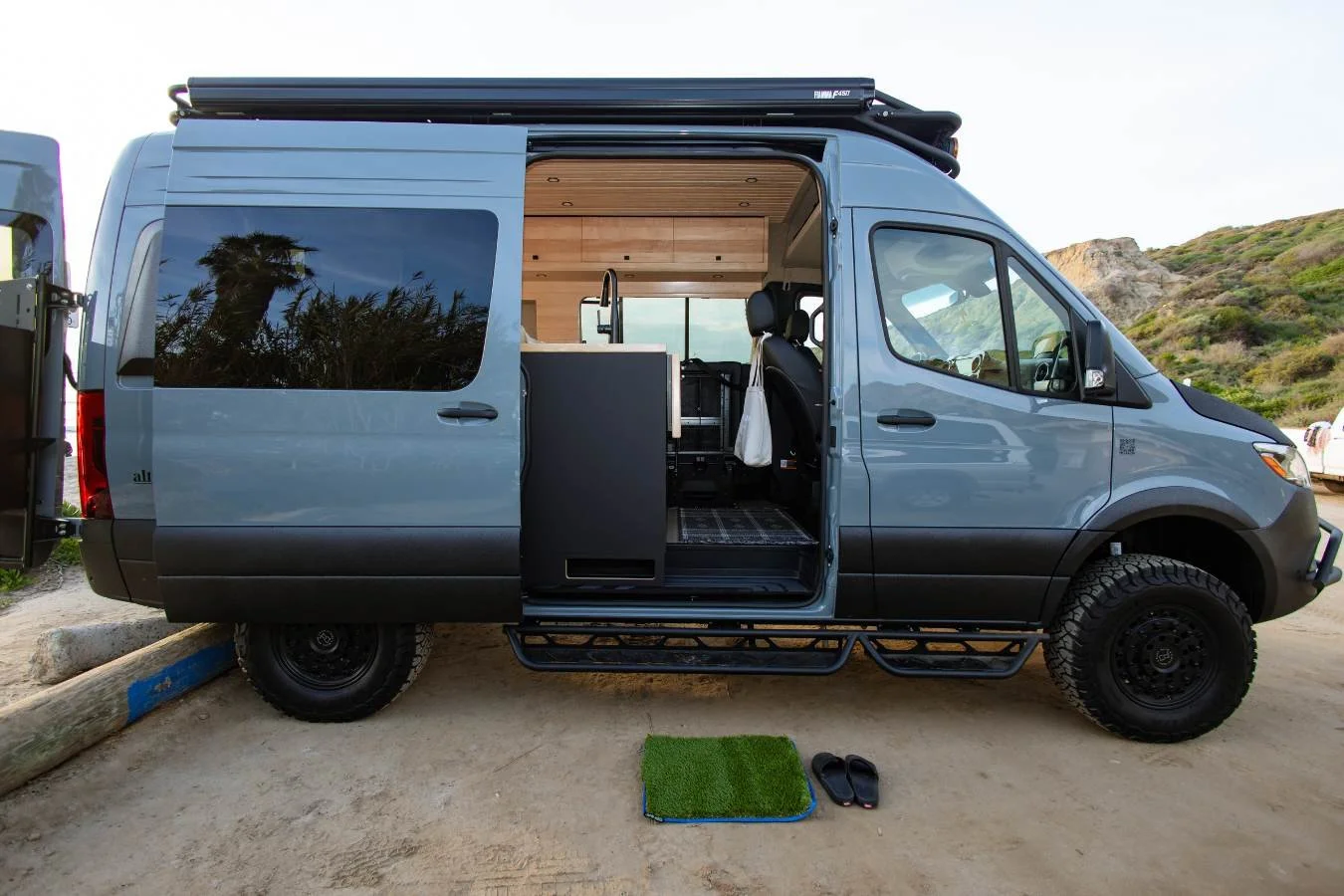 Luxury Mercedes Sprinter camper van with sliding door open at beach campsite