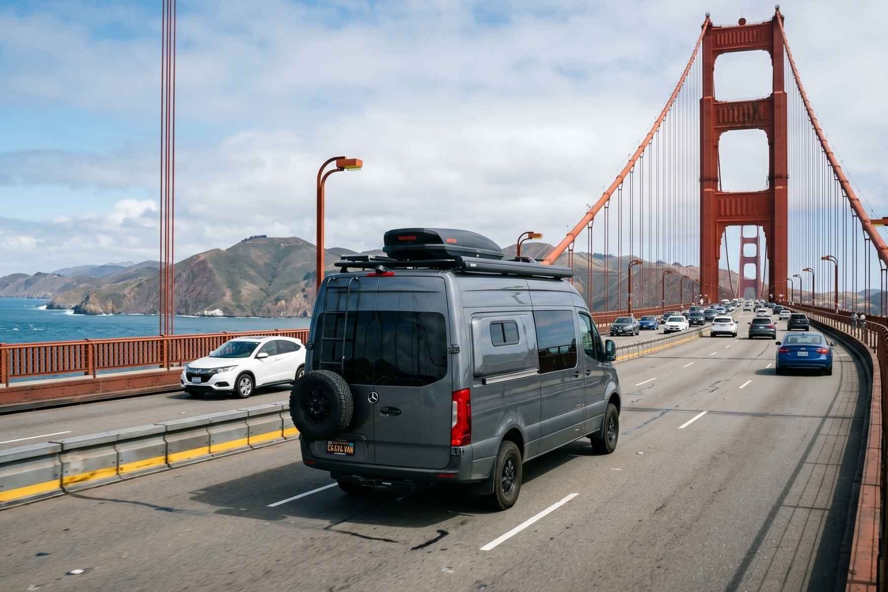 A gray Mercedes Sprinter camper van rental drives across the Golden Gate Bridge in San Francisco with other traffic under a partly cloudy sky.