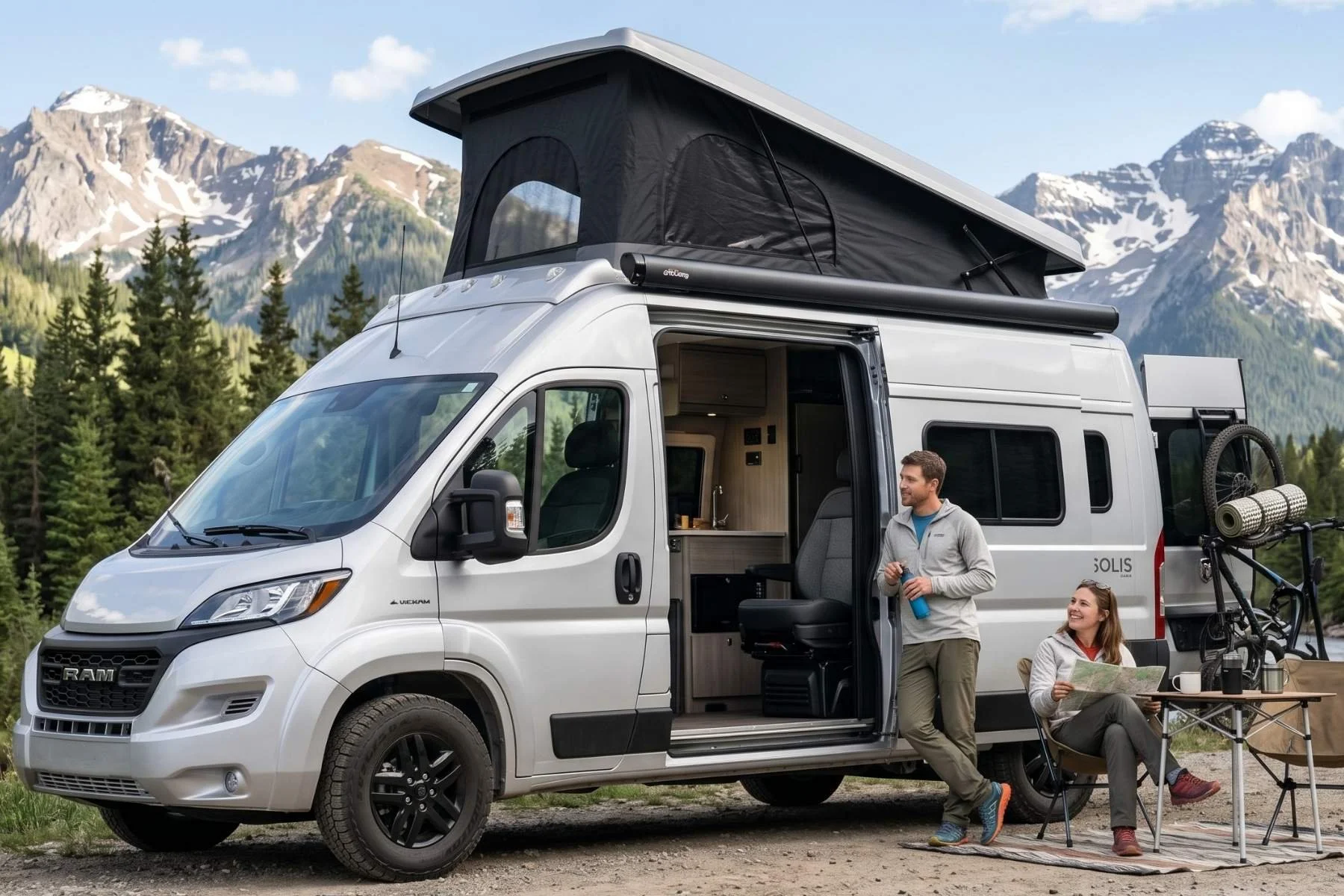 A silver Winnebago Solis camper van with its pop-top roof extended, parked in a scenic mountain valley near a river with two travelers relaxing at a campsite.