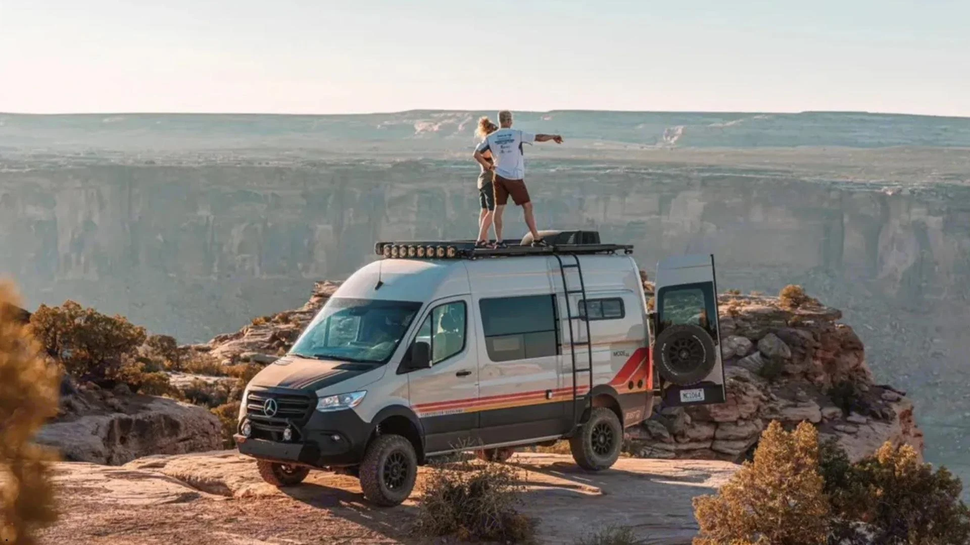 Storyteller Overland Beast Mode 4x4 Sprinter van rental parked on a canyon overlook with two people standing on the roof rack
