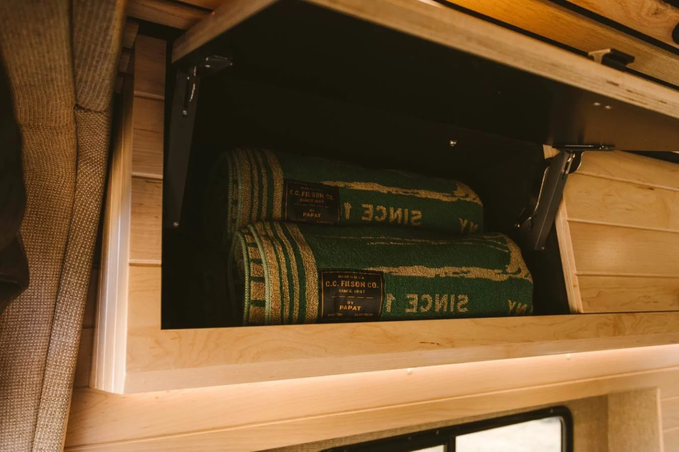 Built-in overhead storage compartment with blankets in camper van interior.