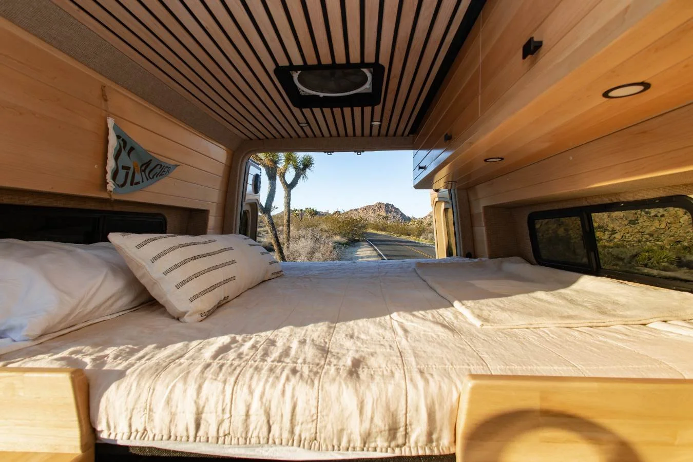 Spacious rear sleeping area with wood ceiling in luxury Sprinter camper van rental.